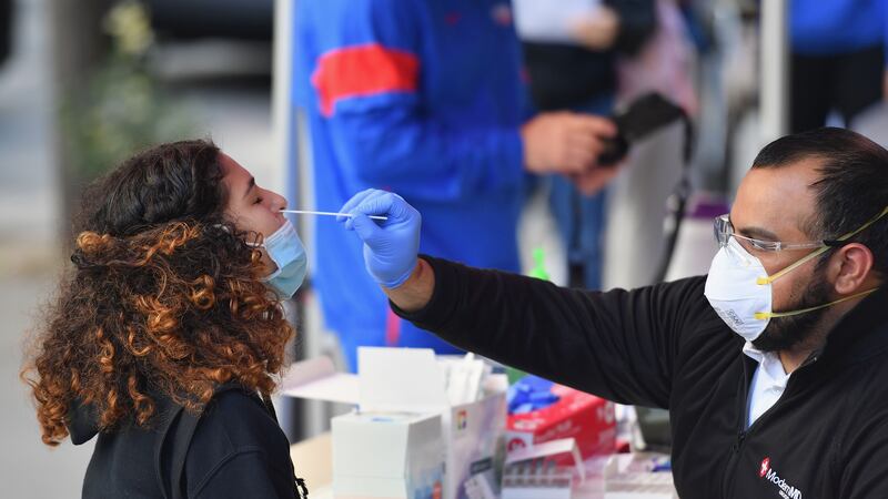 A student wearing a blue face mask is tested for COVID by a medical professional via nasal swab.