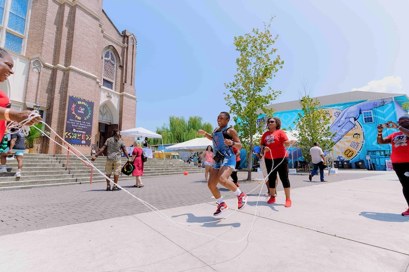 A photograph of a small group of Black adults jump roping outside on a sunny day.