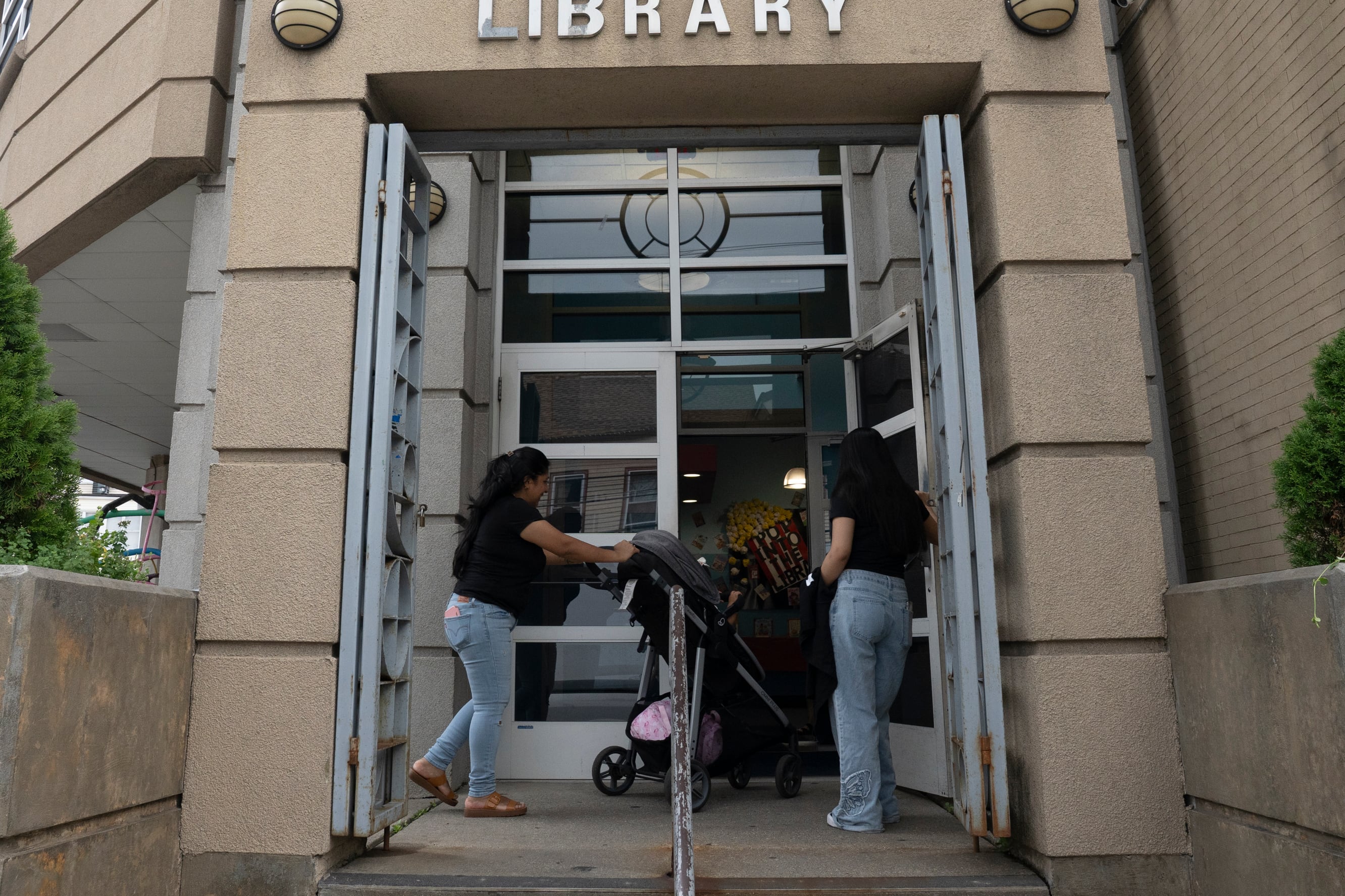 A woman is pushing a baby stroller and walking into a brown-yellowish building.