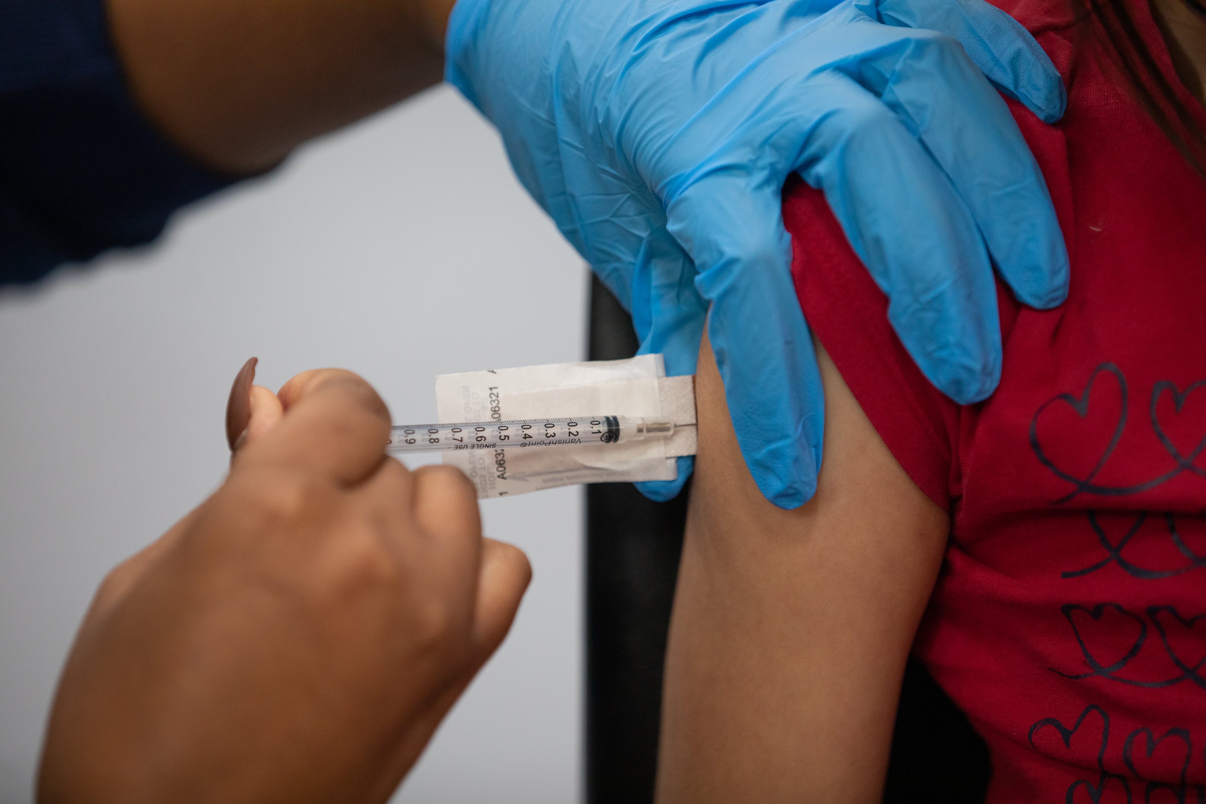 A medical professional gives a shot in the arm to a child in a red t-shirt.