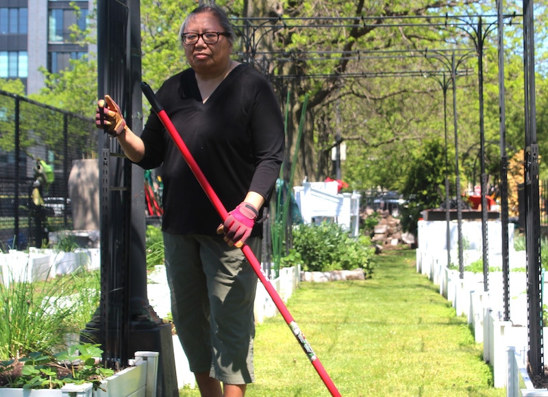 A woman holding a red broom poses for a portrait outside with green trees and poles in the background.