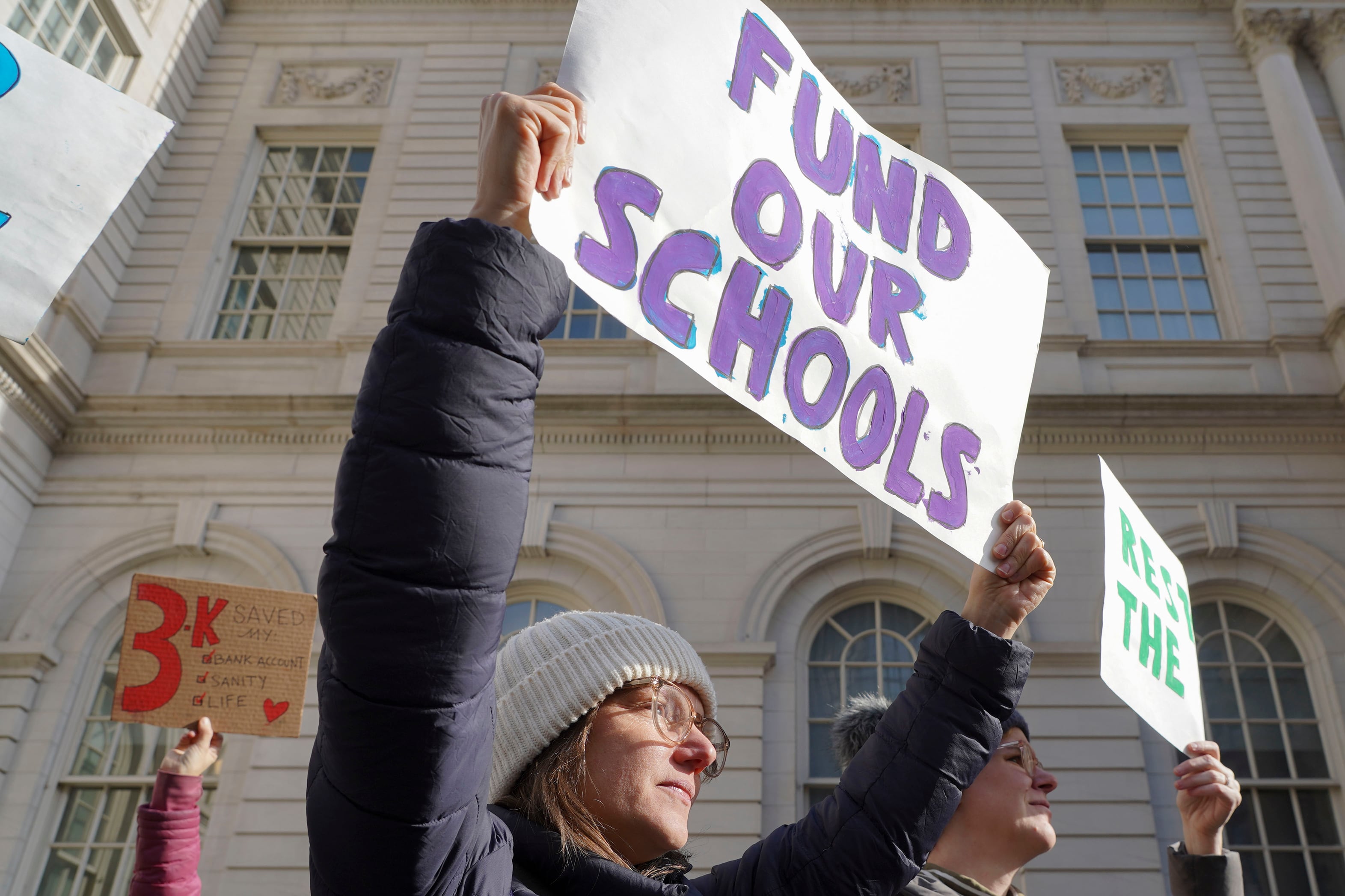 Two people hold up large signs outside of a large white stone building.