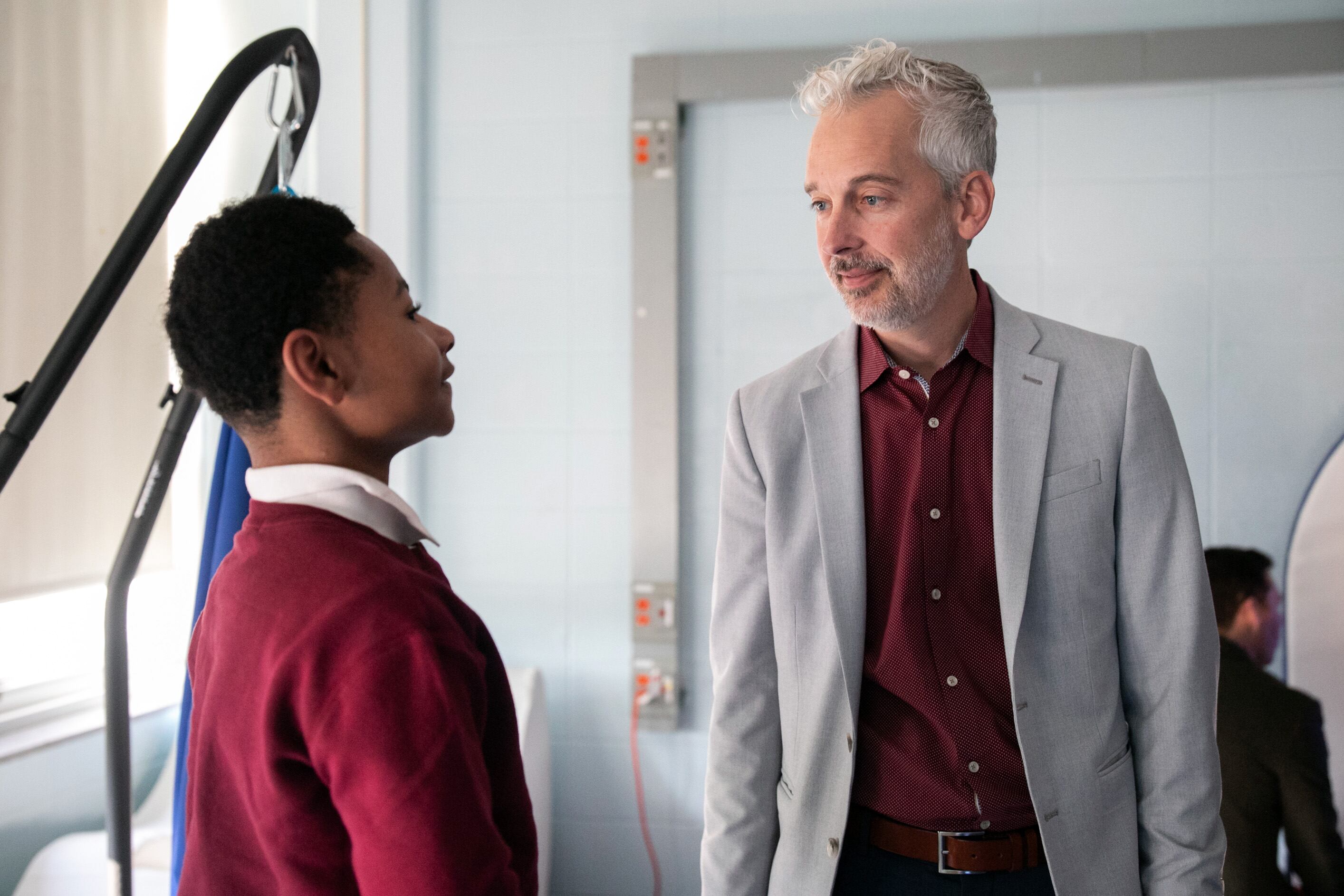 An adult in a suit and a young student stand in a classroom.