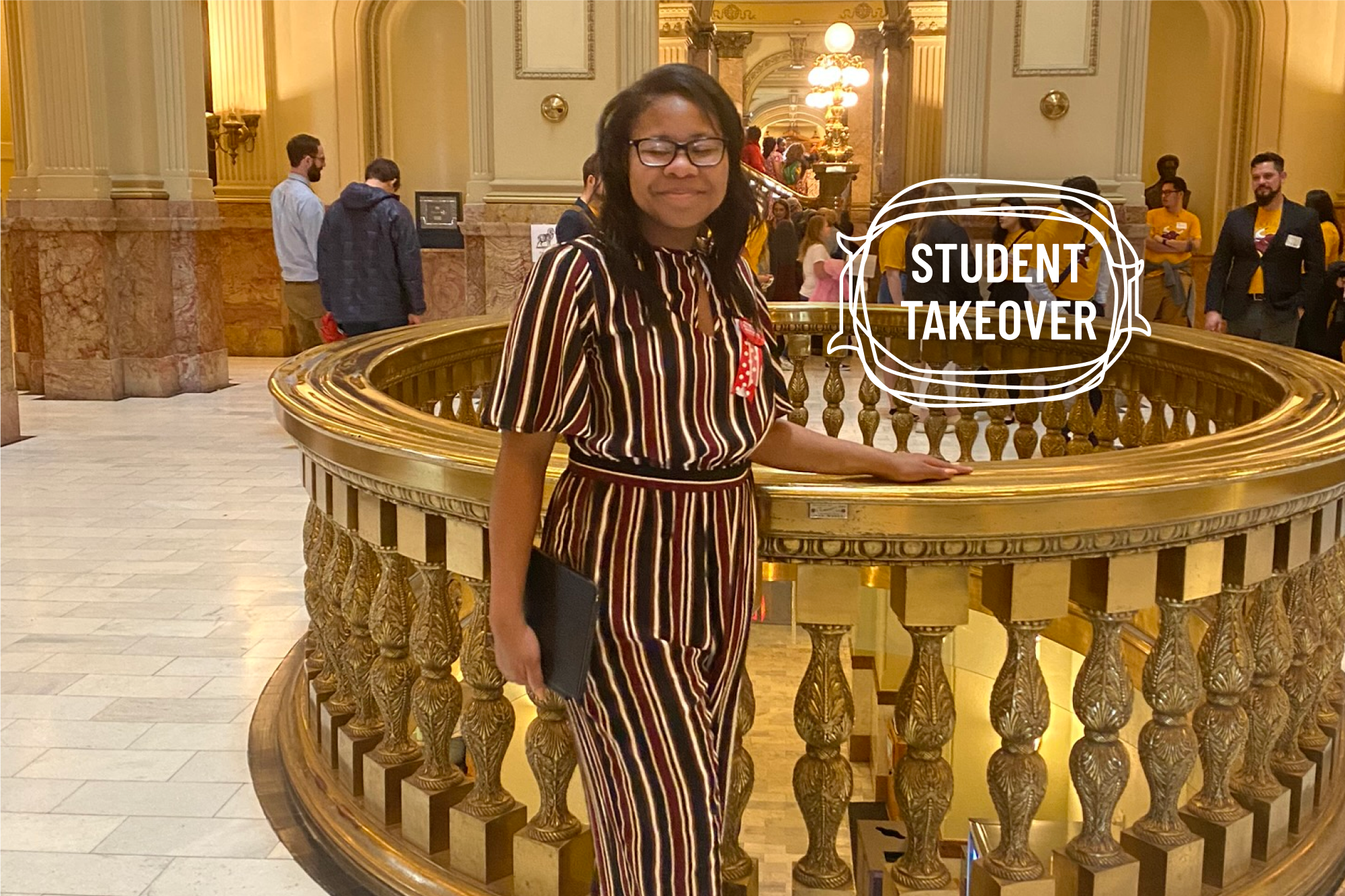 Jayla Hemphill wearing a striped jumpsuit, standing next to an ornate gold hand-railing smiling.