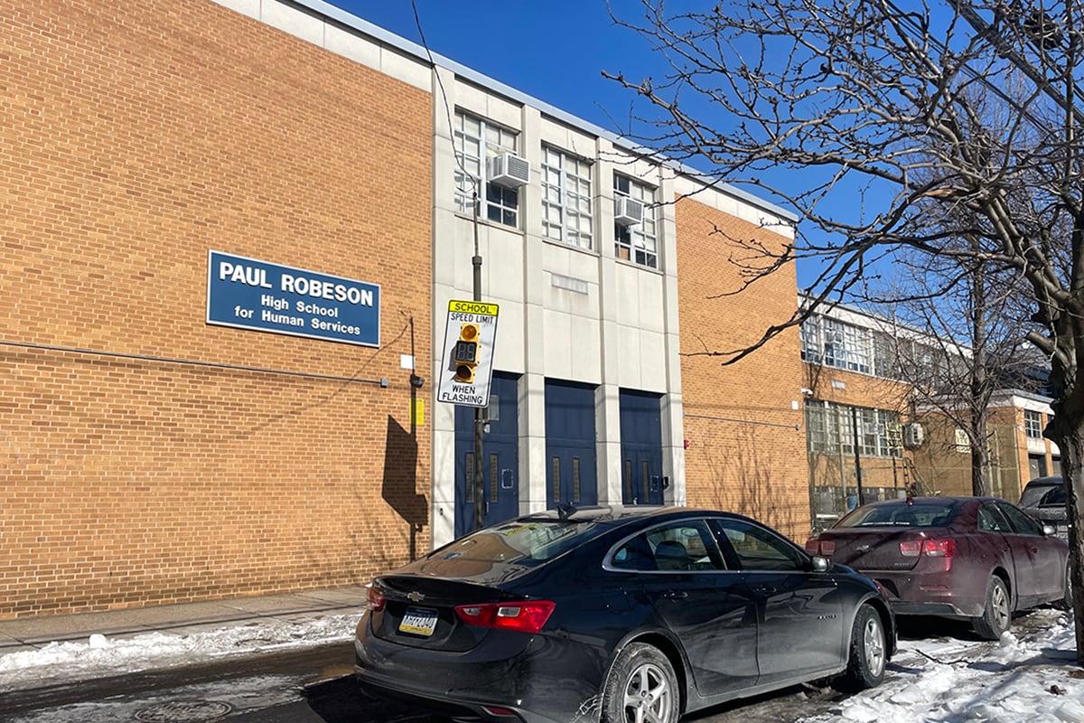 A school name sign hangs on a brick building.