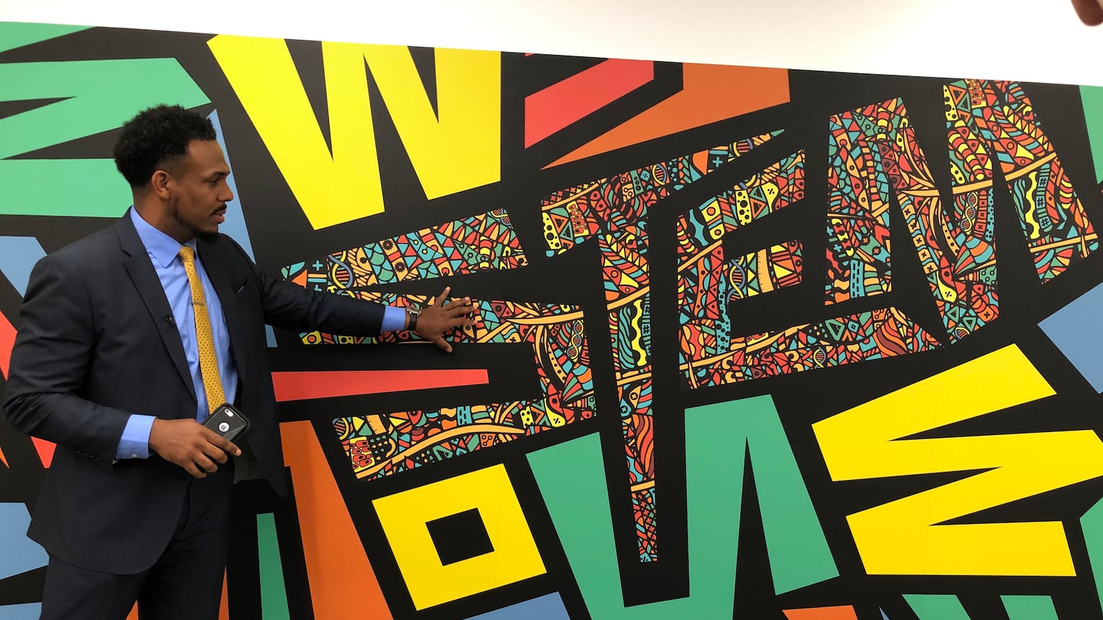Principal Conrad Timbers-Ausar stands in front of a mural at the new Englewood STEM high school.