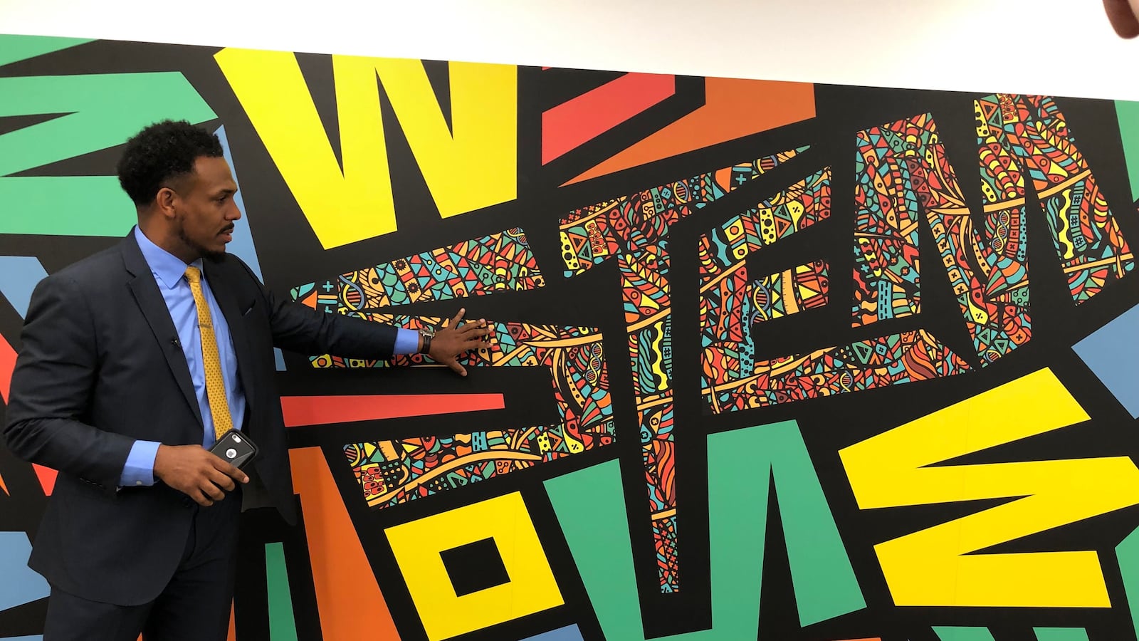 Principal Conrad Timbers-Ausar stands in front of a mural at the new Englewood STEM high school.