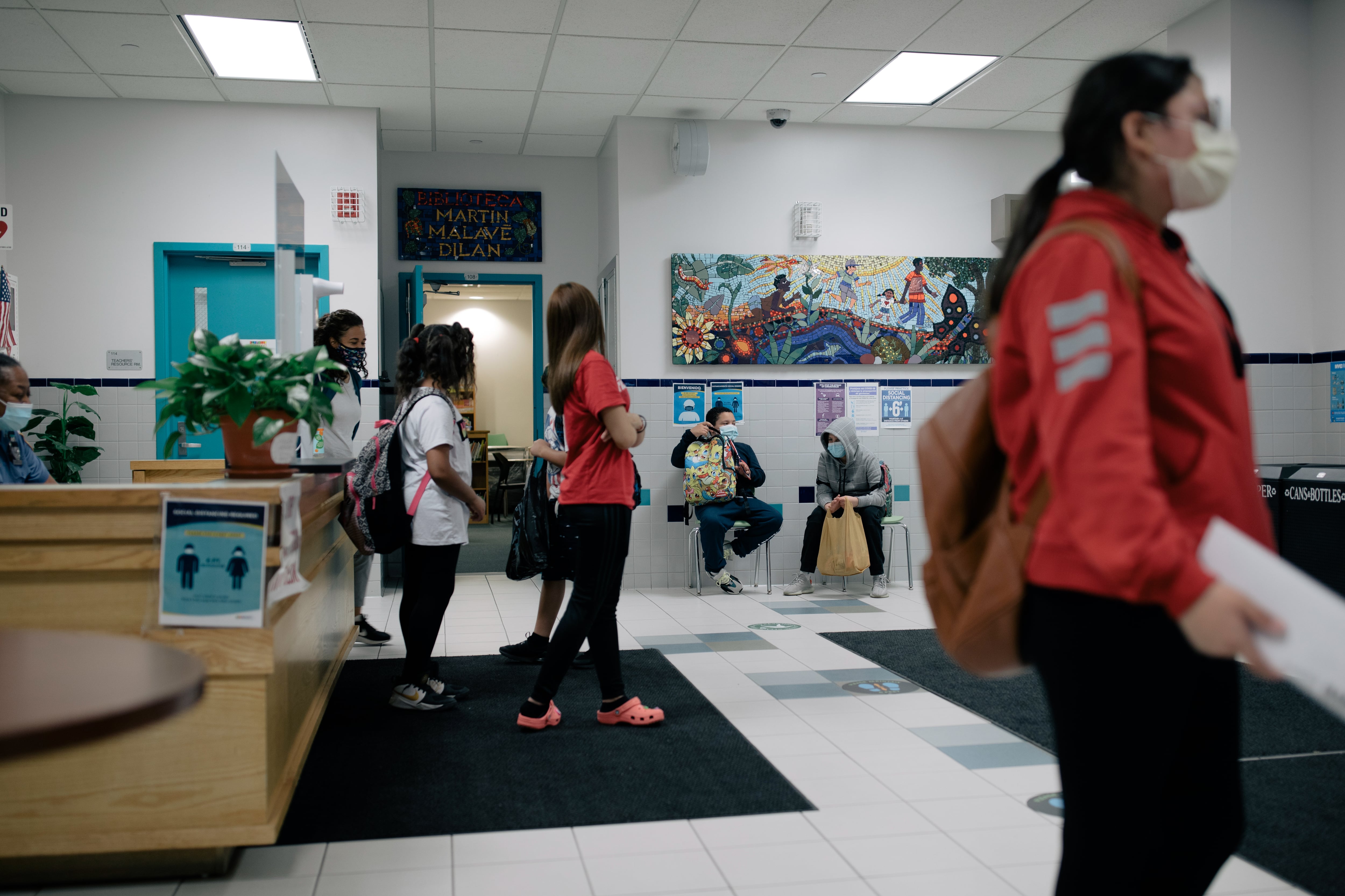 Students walk through the lobby of P.S. 89, with ornate murals on the walls and light blue doors.