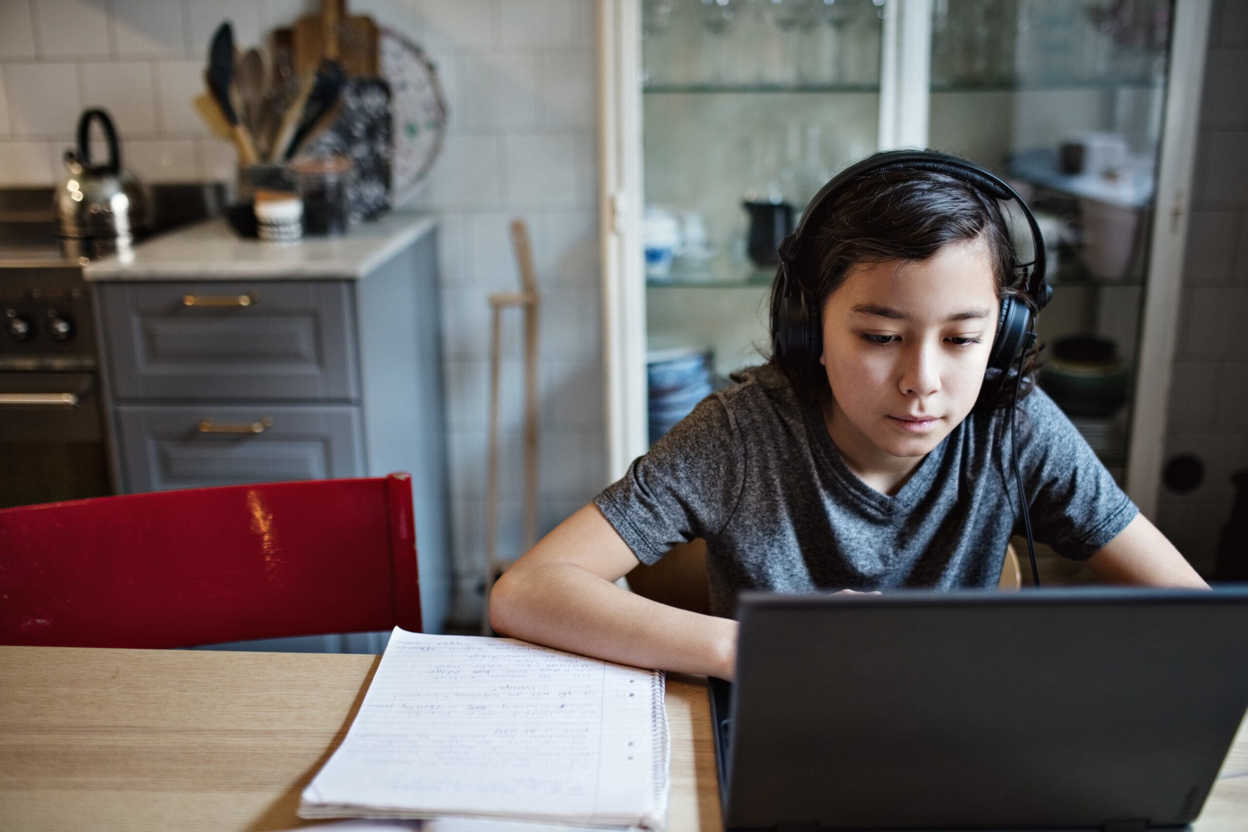 Boy wearing headphones while using laptop during homework at home.