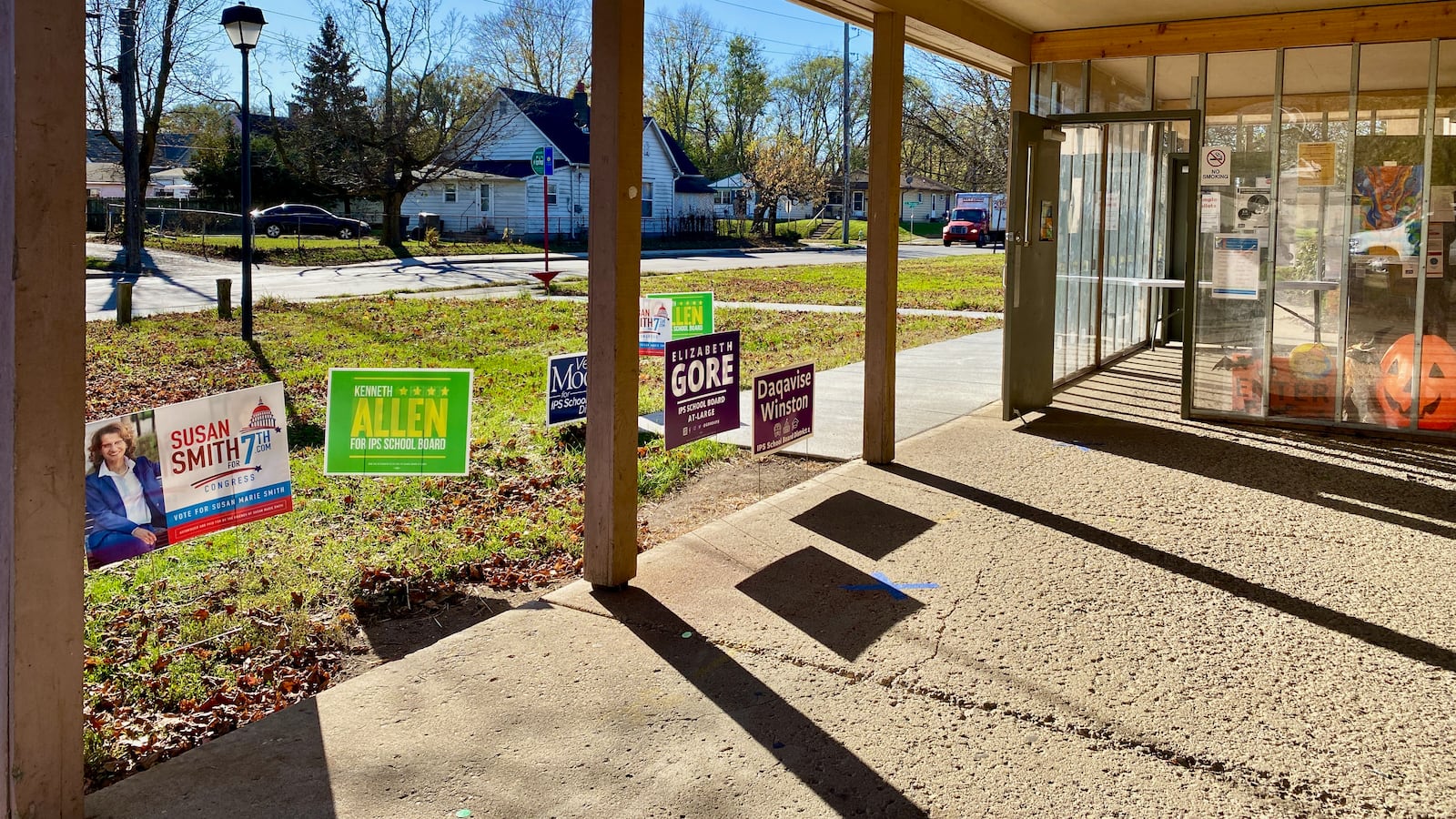 Political signs are standing in the ground by the door to a building that is a polling location.