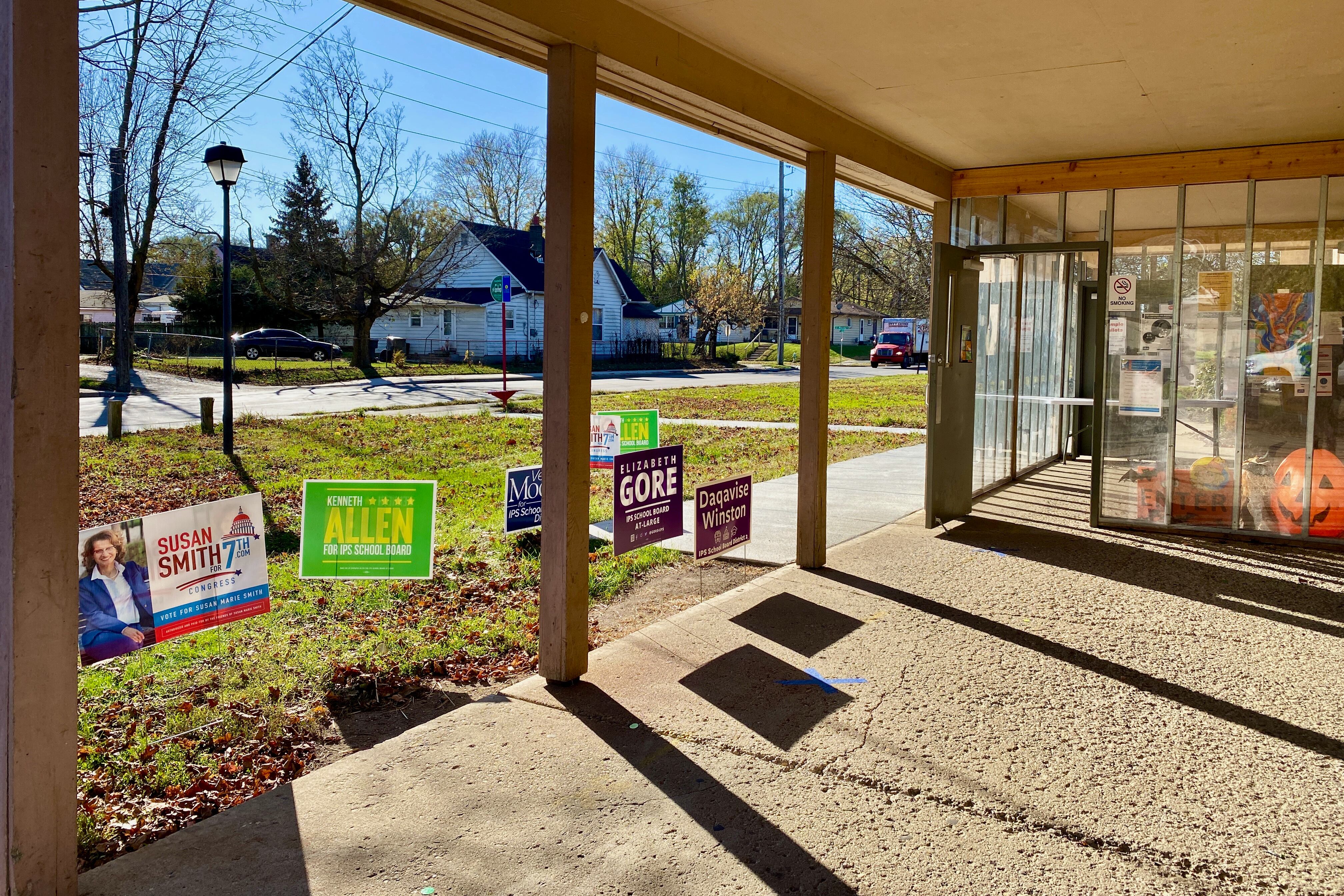 Political signs are standing in the ground by the door to a building that is a polling location.