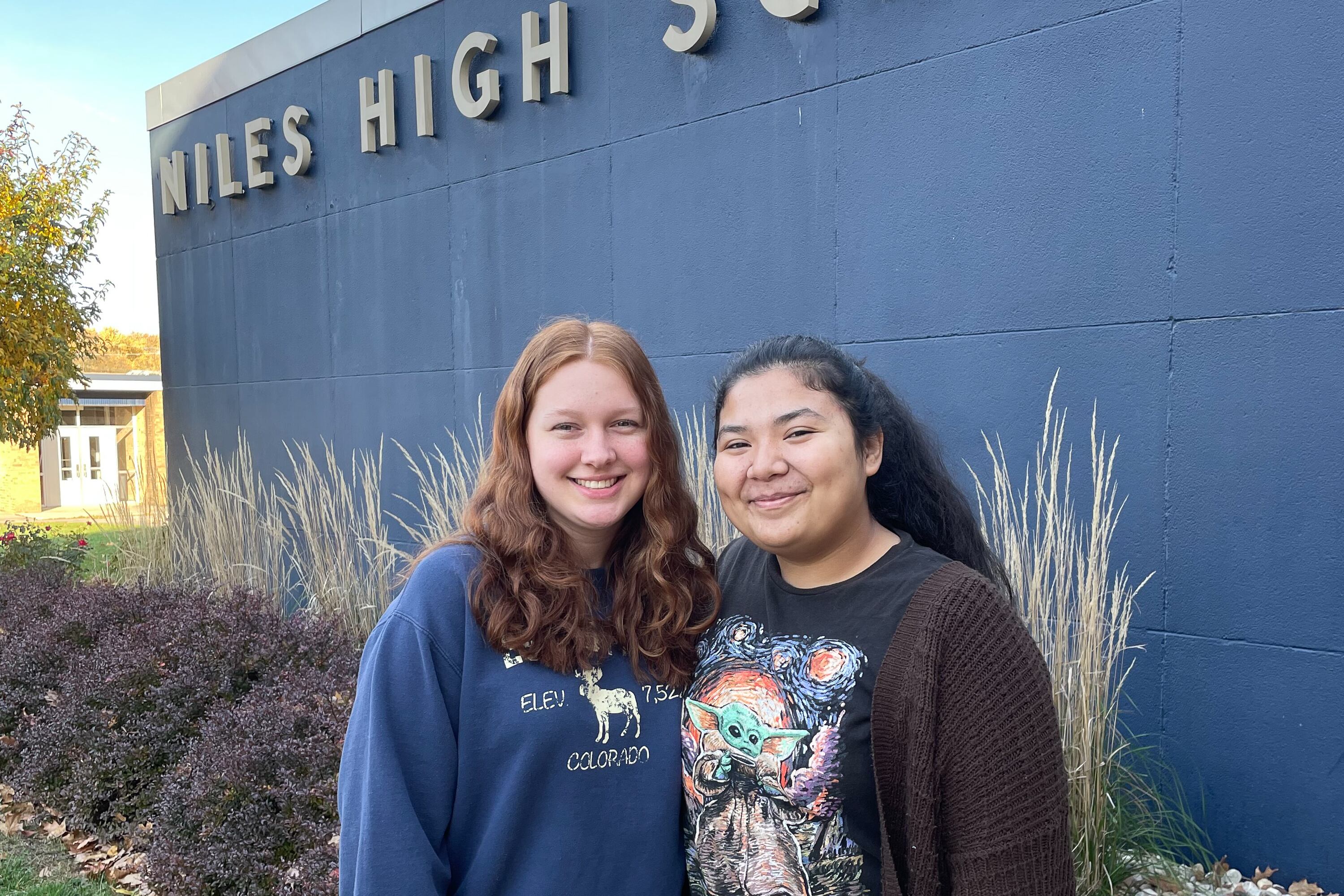 Two teenage girls stand outside Niles High School on a sunny day. 