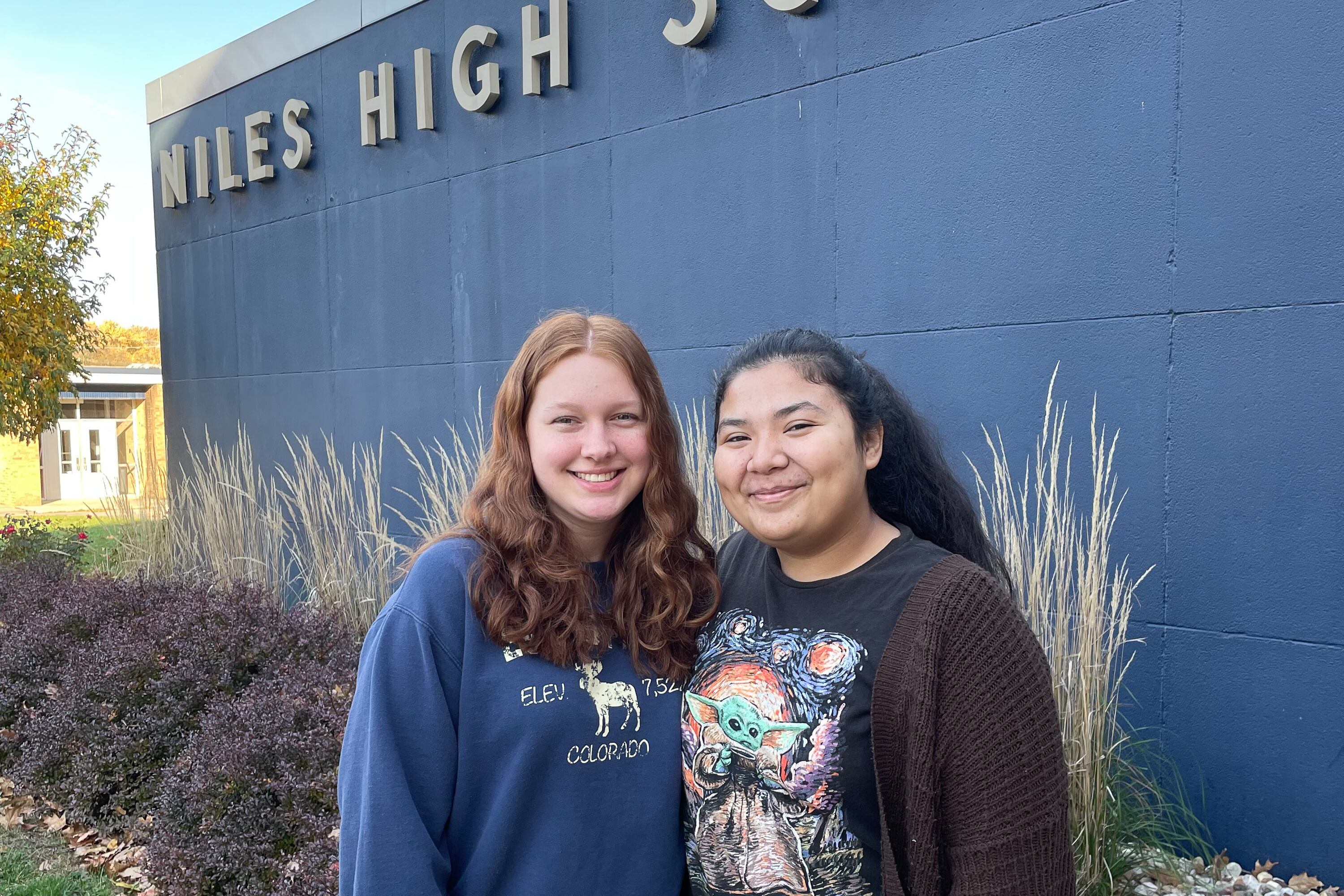 Two teenage girls stand outside Niles High School on a sunny day.