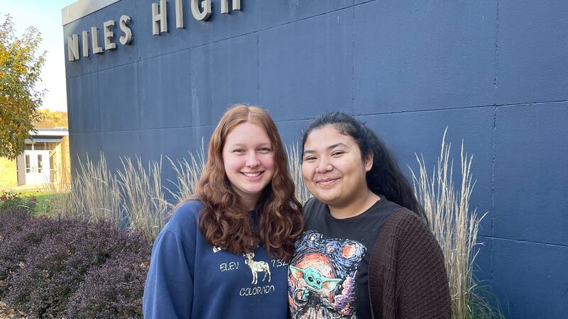 Two teenage girls stand outside Niles High School on a sunny day. 