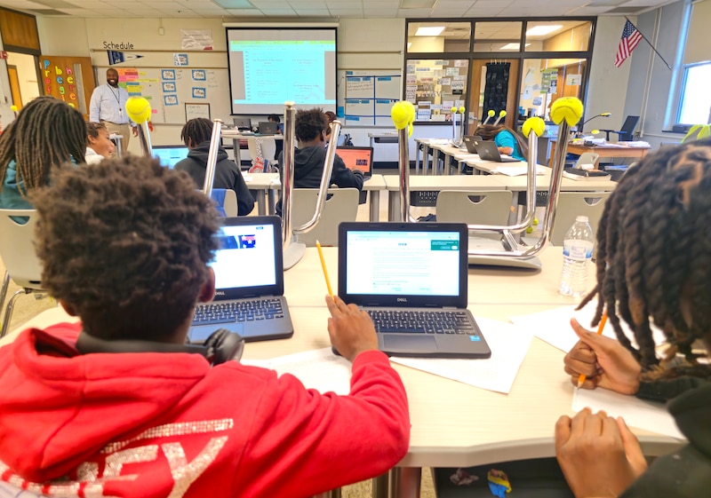 Students work from their desks on laptops in a classroom.