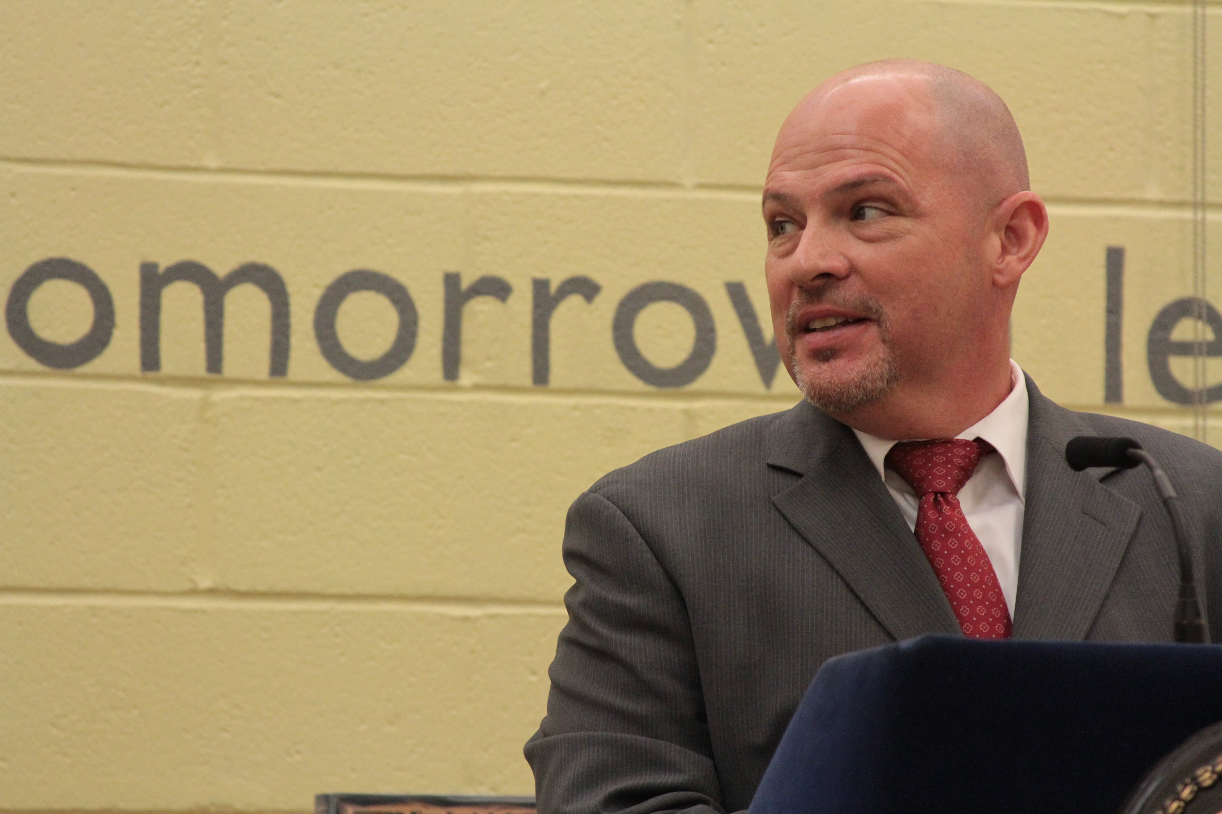 A man in a gray suit and red tie stands at a podium.