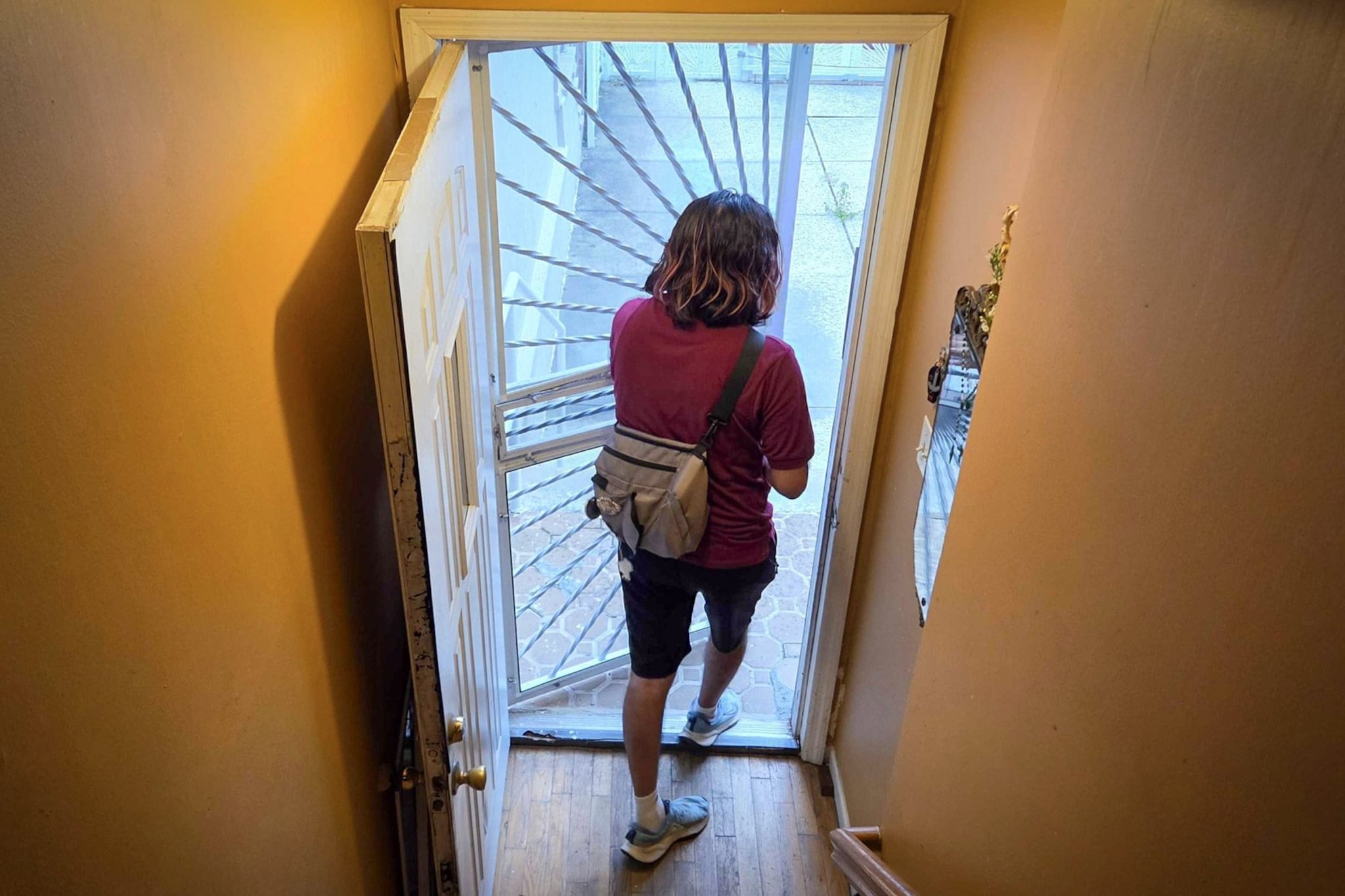 A boy with shoulder-length hair walks out the door of a house.