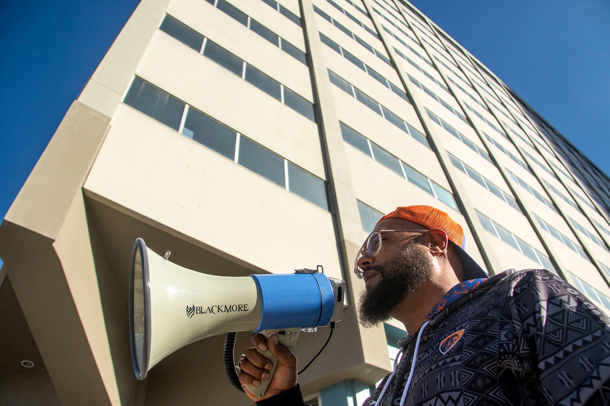 A man speaks into a bullhorn. A high-rise building looms behind him.