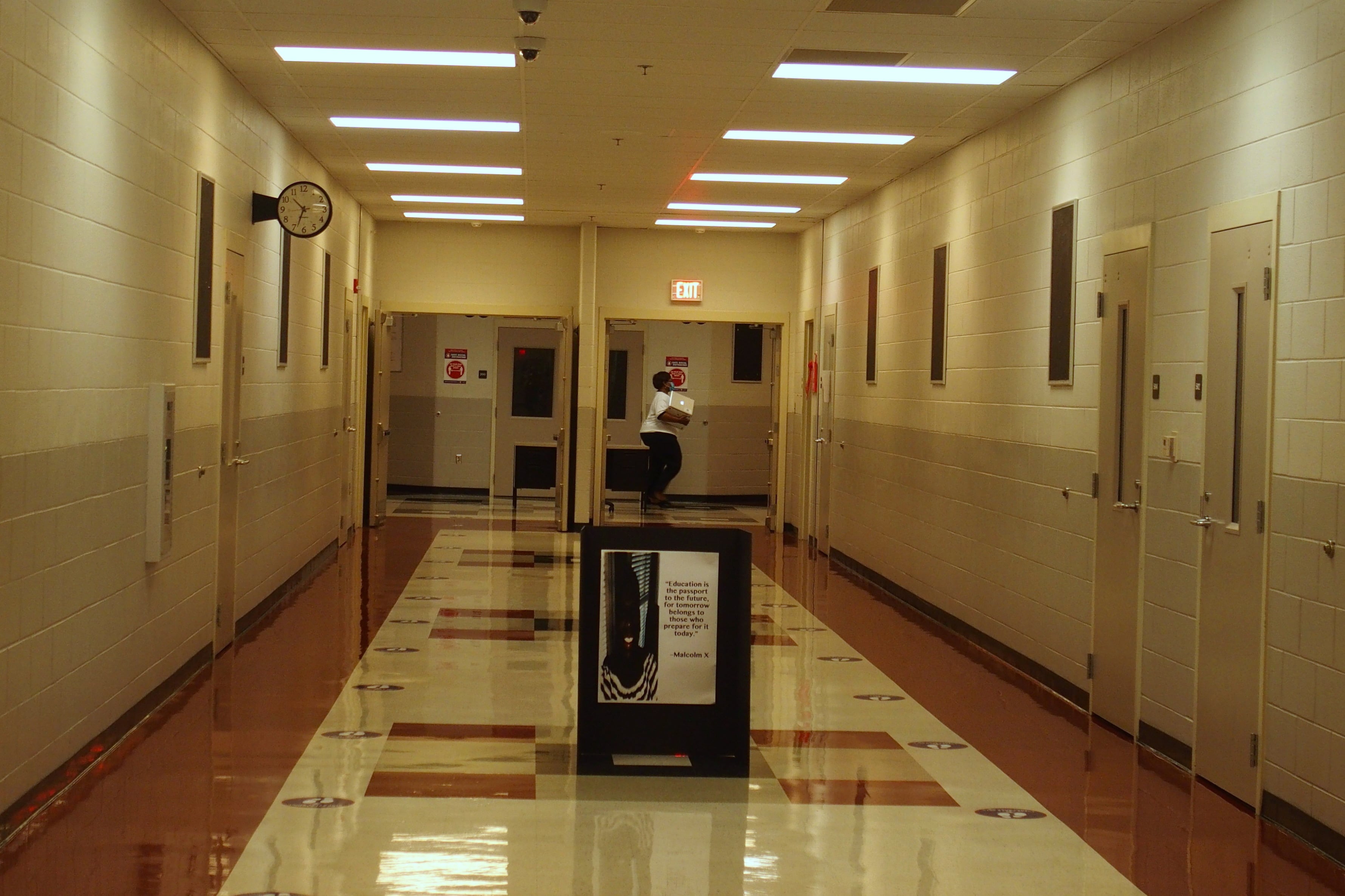 A teacher crosses an otherwise empty hallway with stickers on the floor promoting social distancing