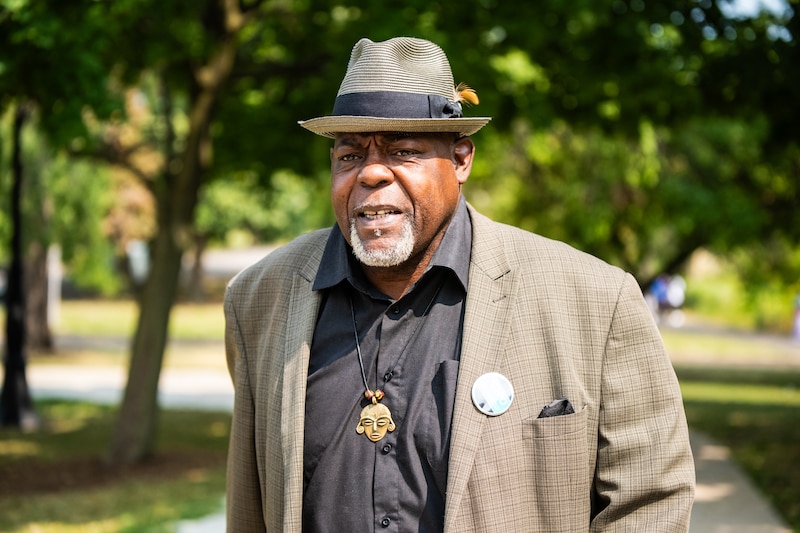 A man in a gray jacket, black shirt and hat.