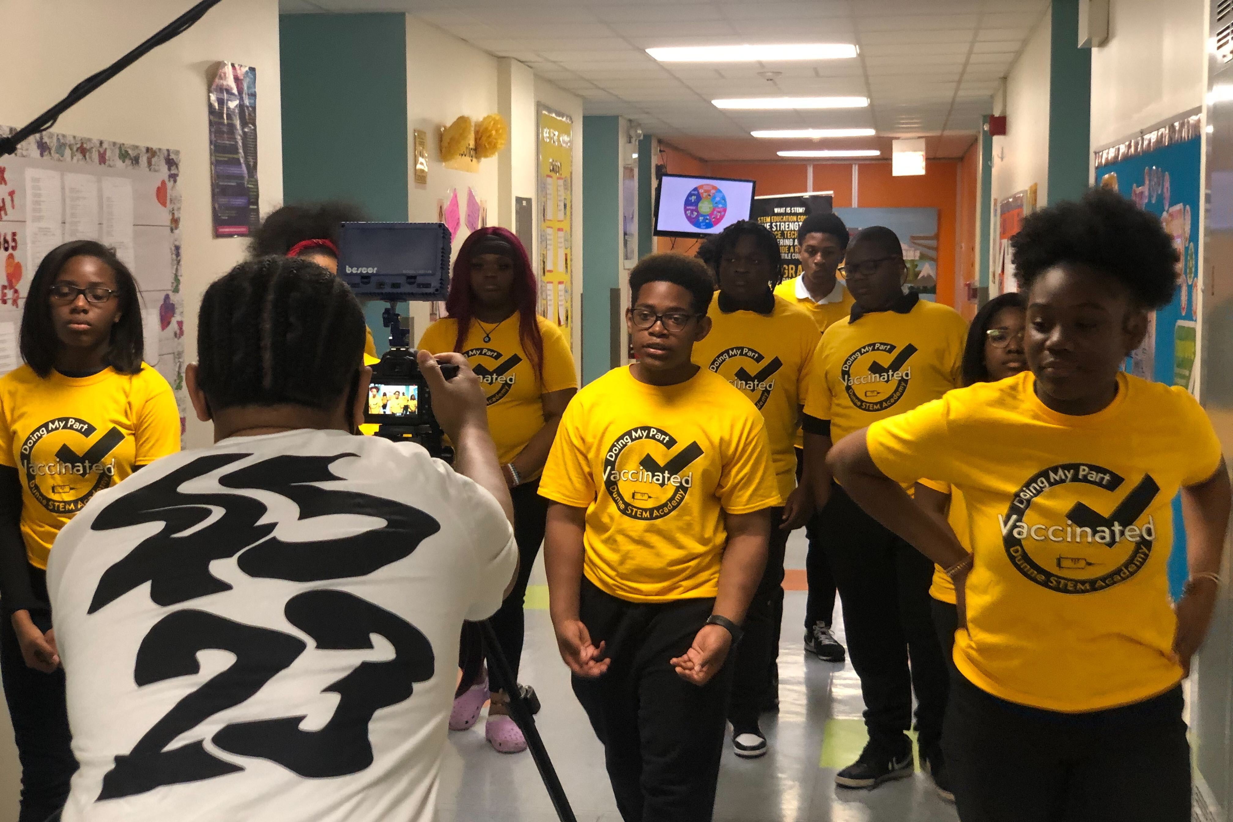 A group of students walk down a school hallway wearing bright yellow shirts that say: “Doing my part. Vaccinated.”