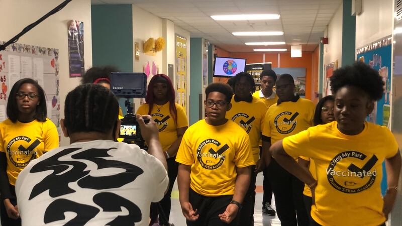 A group of students walk down a school hallway wearing bright yellow shirts that say: “Doing my part. Vaccinated.”