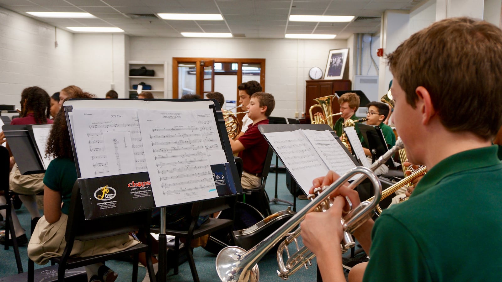 Middle school students practice the trumpet, tuba, French horn and other instruments in a classroom