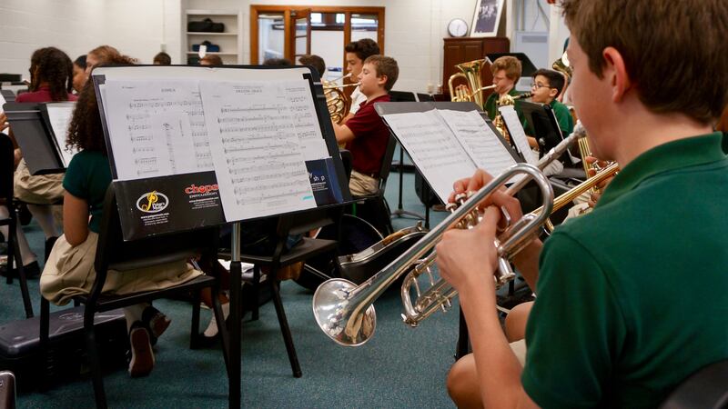 Middle school students practice the trumpet, tuba, French horn and other instruments in a classroom