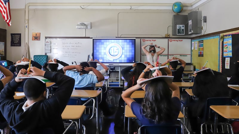 Students and their teacher balance their notebooks on their heads during class on the first day of school.