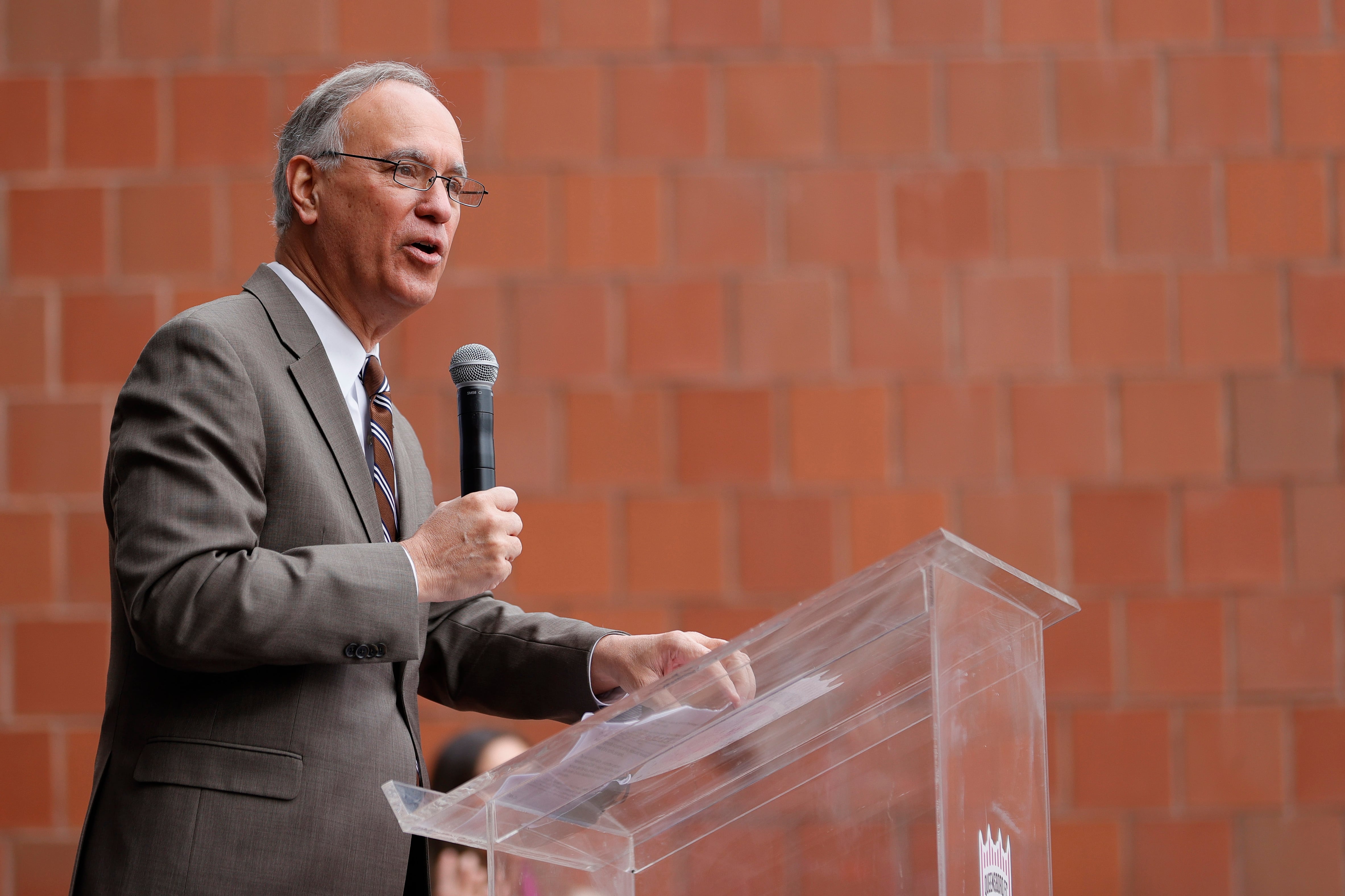 A man in a suit and glasses speaks from a podium.