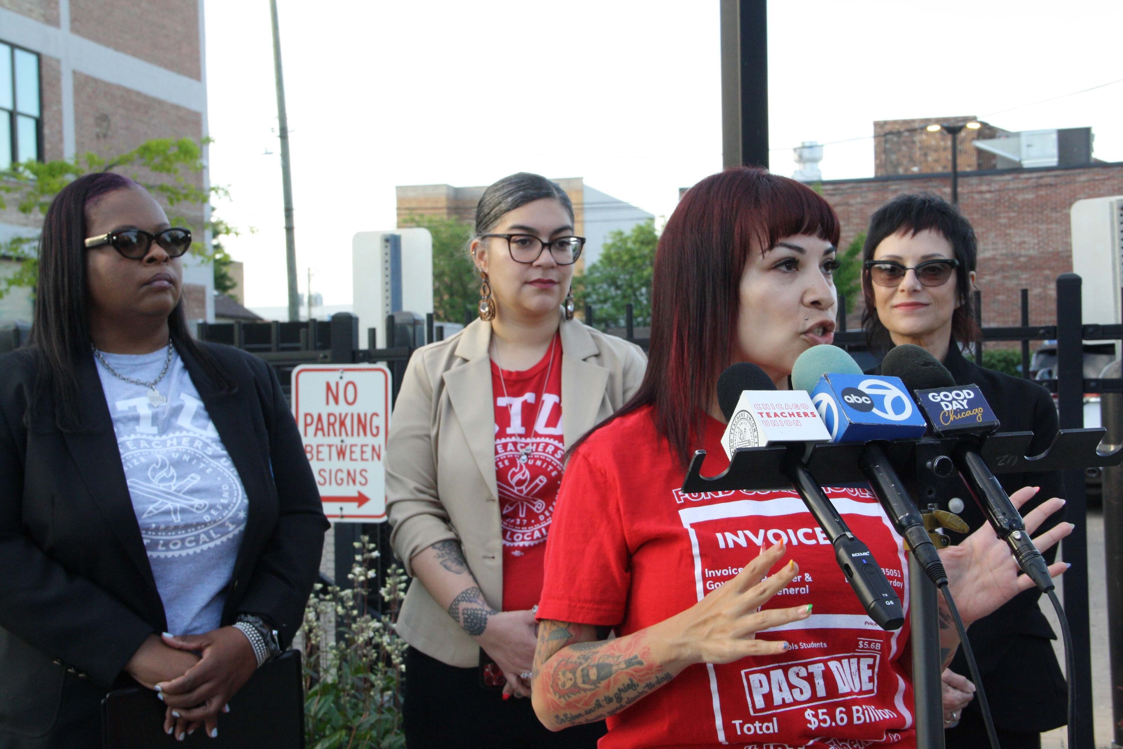 A woman in a red t-shirt speaks in front of microphones.