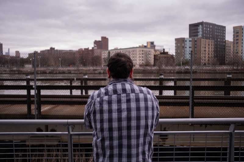 A man's back to the camera as he overlooks buildings along the water.