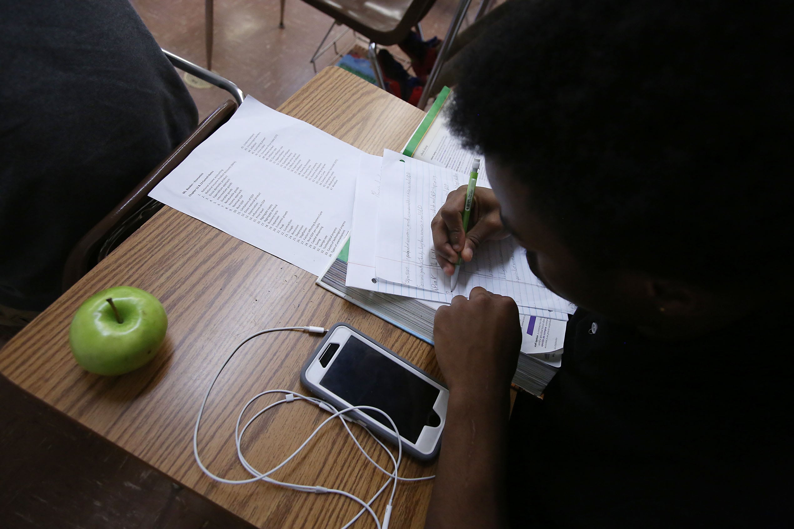 A bird's eye view of a student working at a desk with a green apple and a cellphone.
