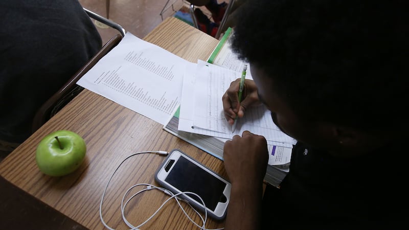 A bird's eye view of a student working at a desk with a green apple and a cellphone.