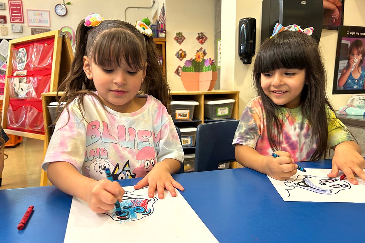 Two girls work at a blue table.