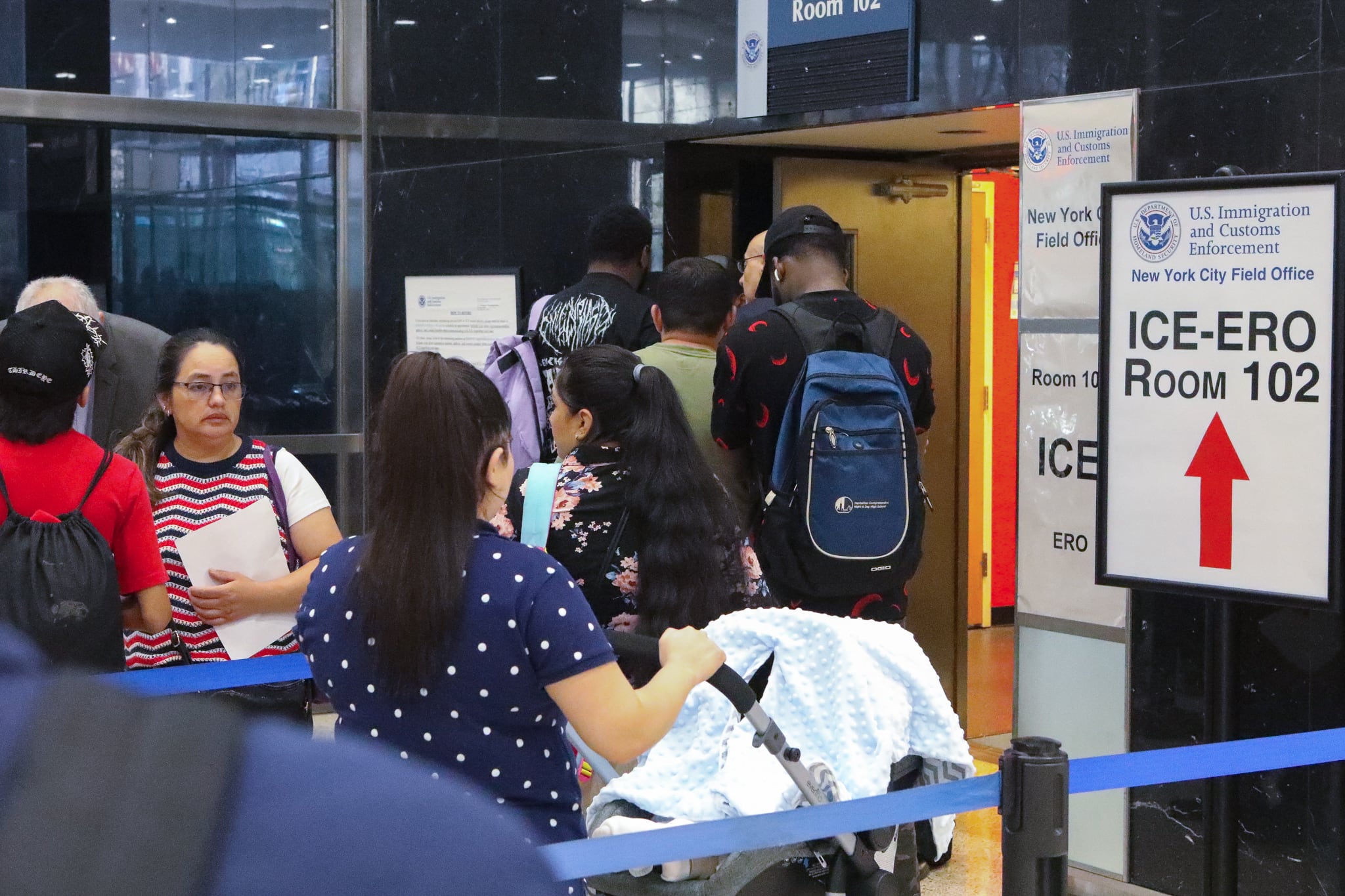 A woman with a baby stroller waits in a snaking line.