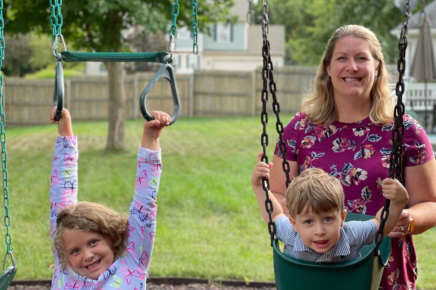A mom smiles behind two children on swings