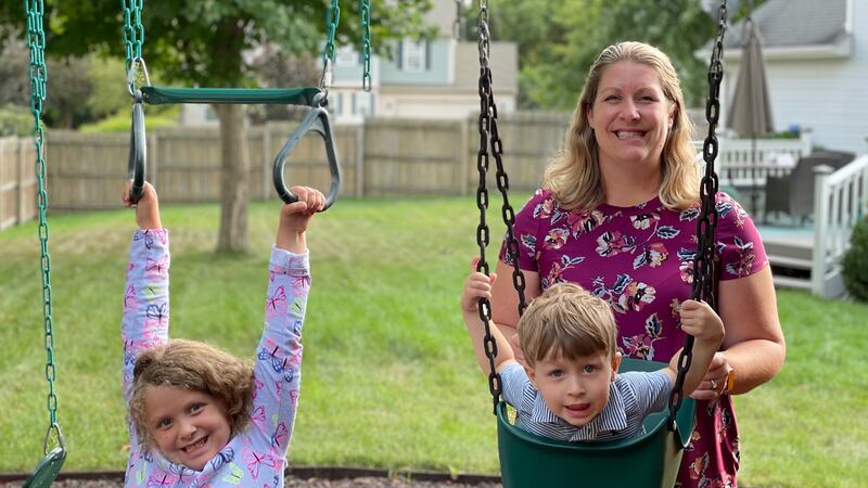 A mom smiles behind two children on swings