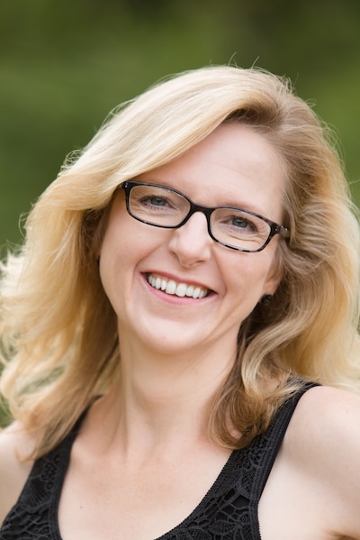 Headshot of a blond woman wearing black glasses and a black tank top.