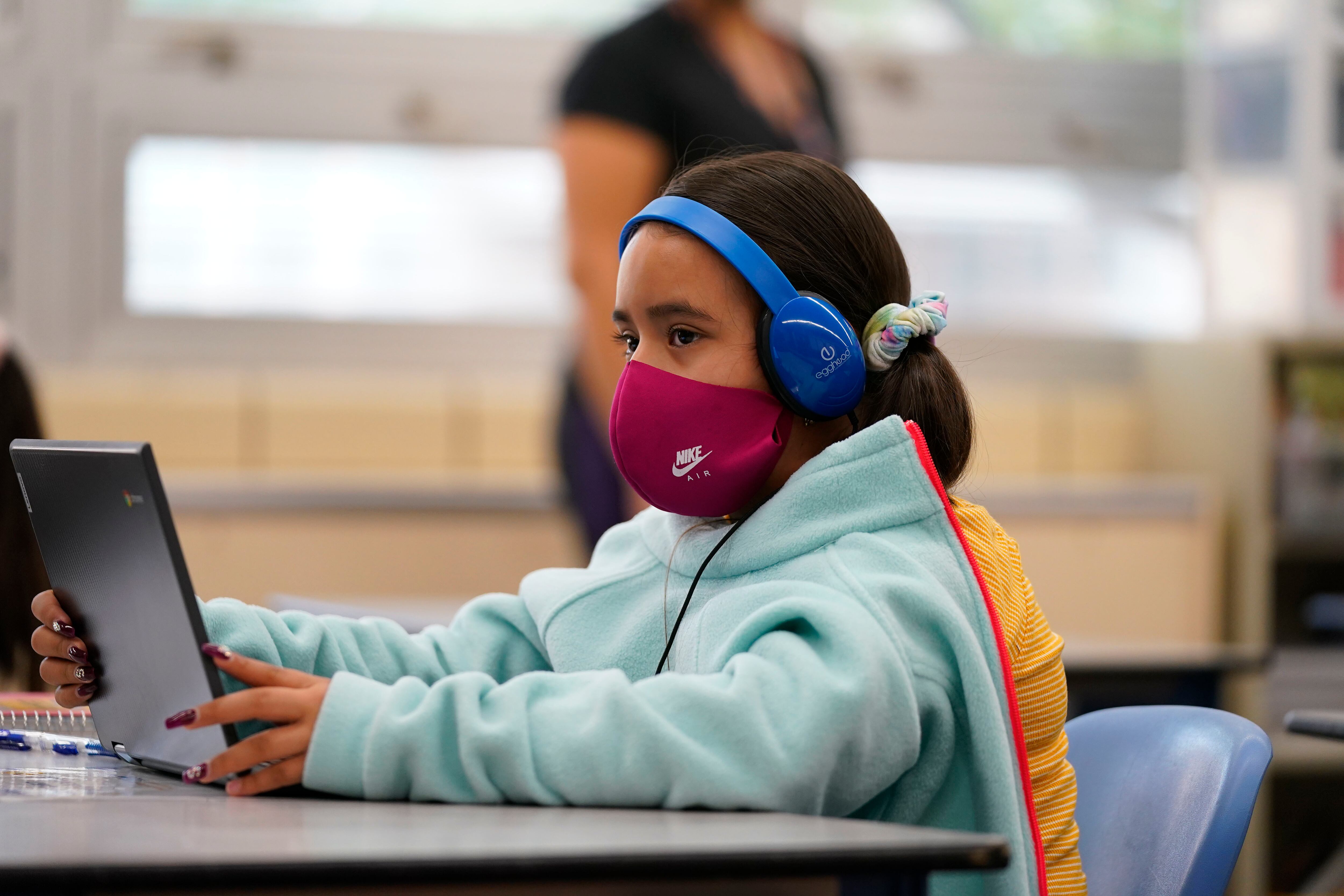 Girl wearing a mask works on her laptop at a learning center.