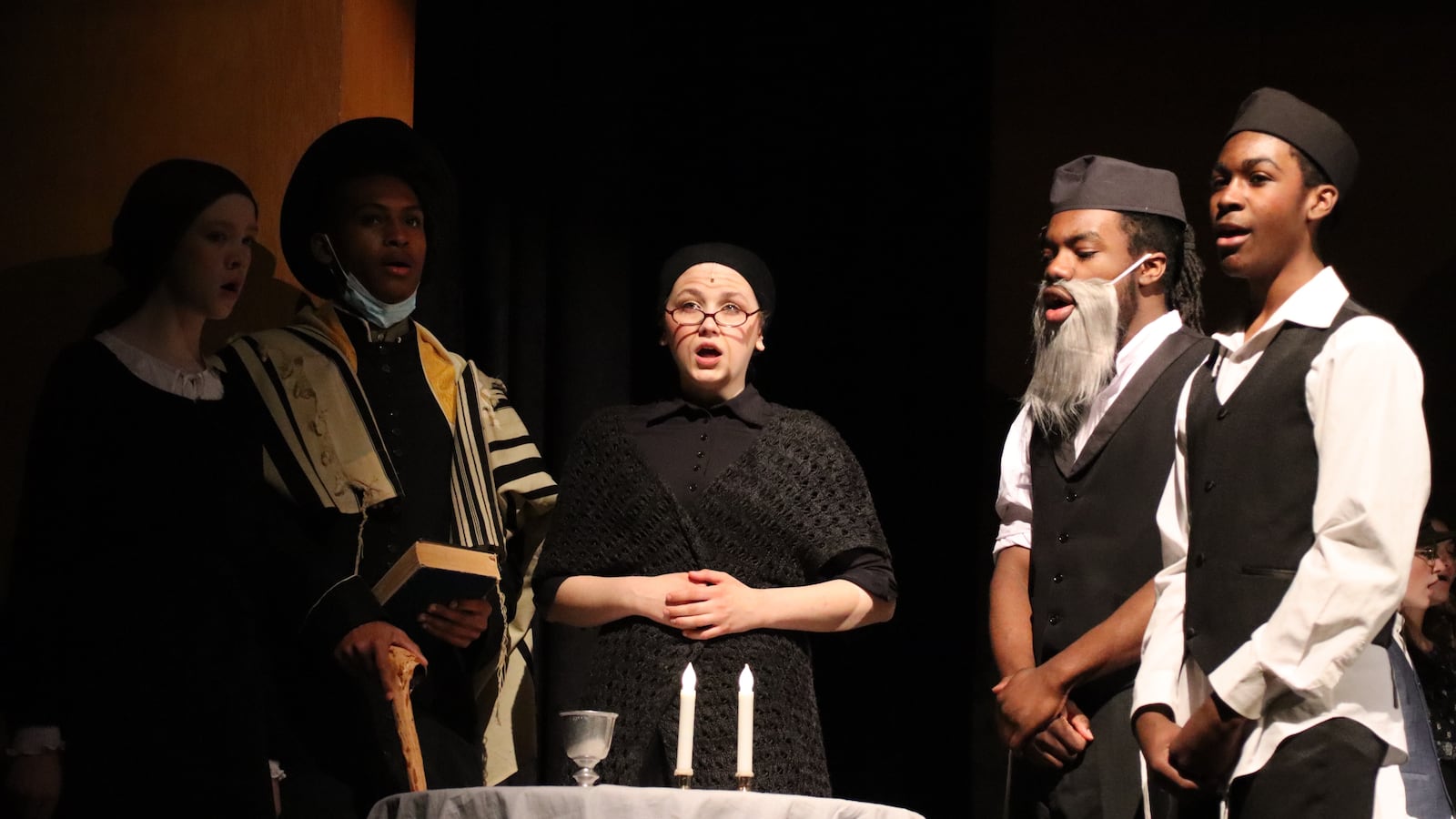 A group of student actors wearing traditional Jewish garb perform a scene in a school play of "Fiddler on the Roof."