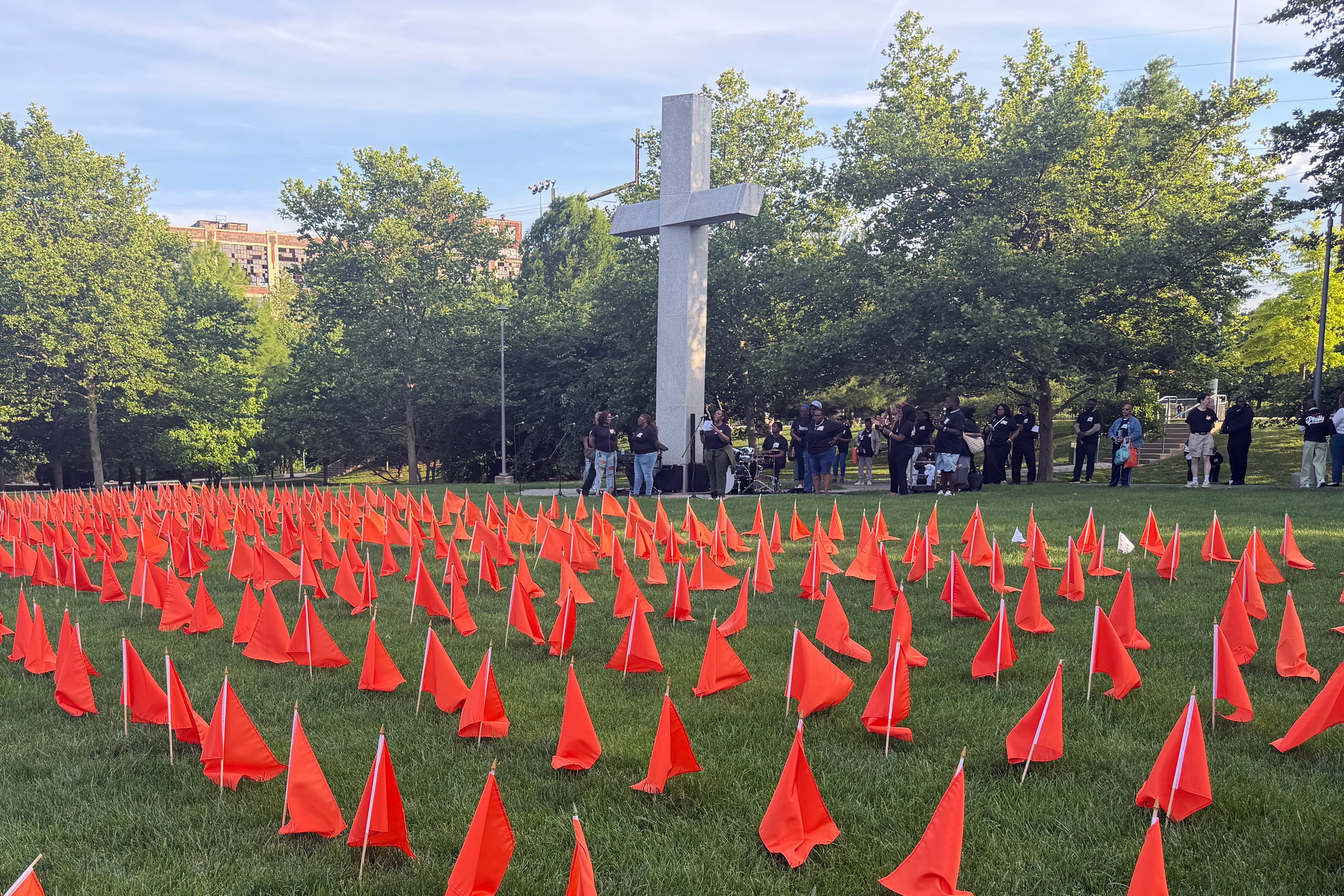 A photograph of a large field full of orange flags with a large stone cross in the background.