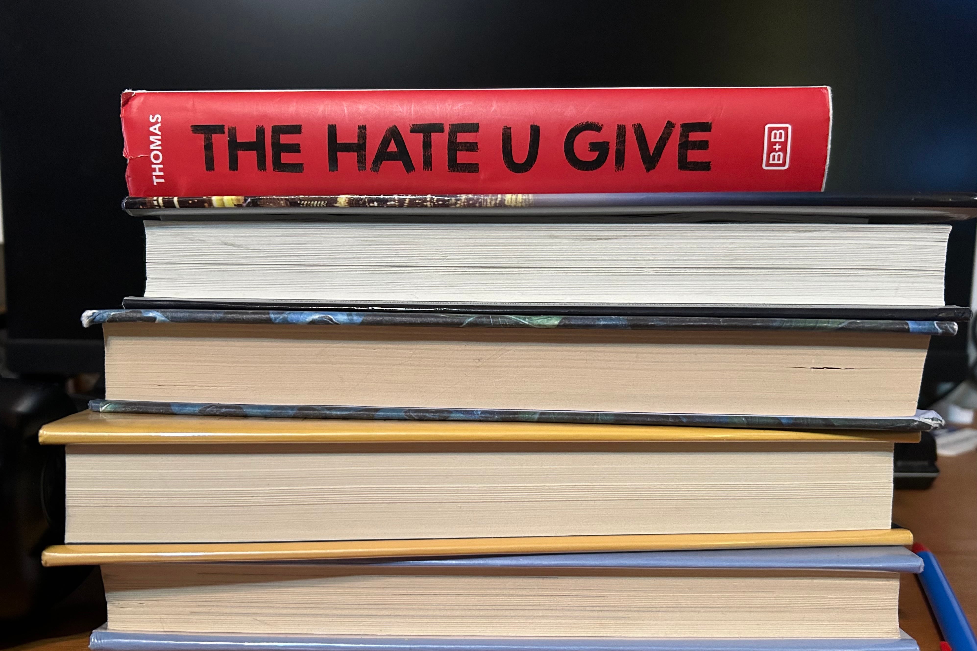 A photograph of five books stacked on top with the top one reading "The Hate U Give" with a dark background.