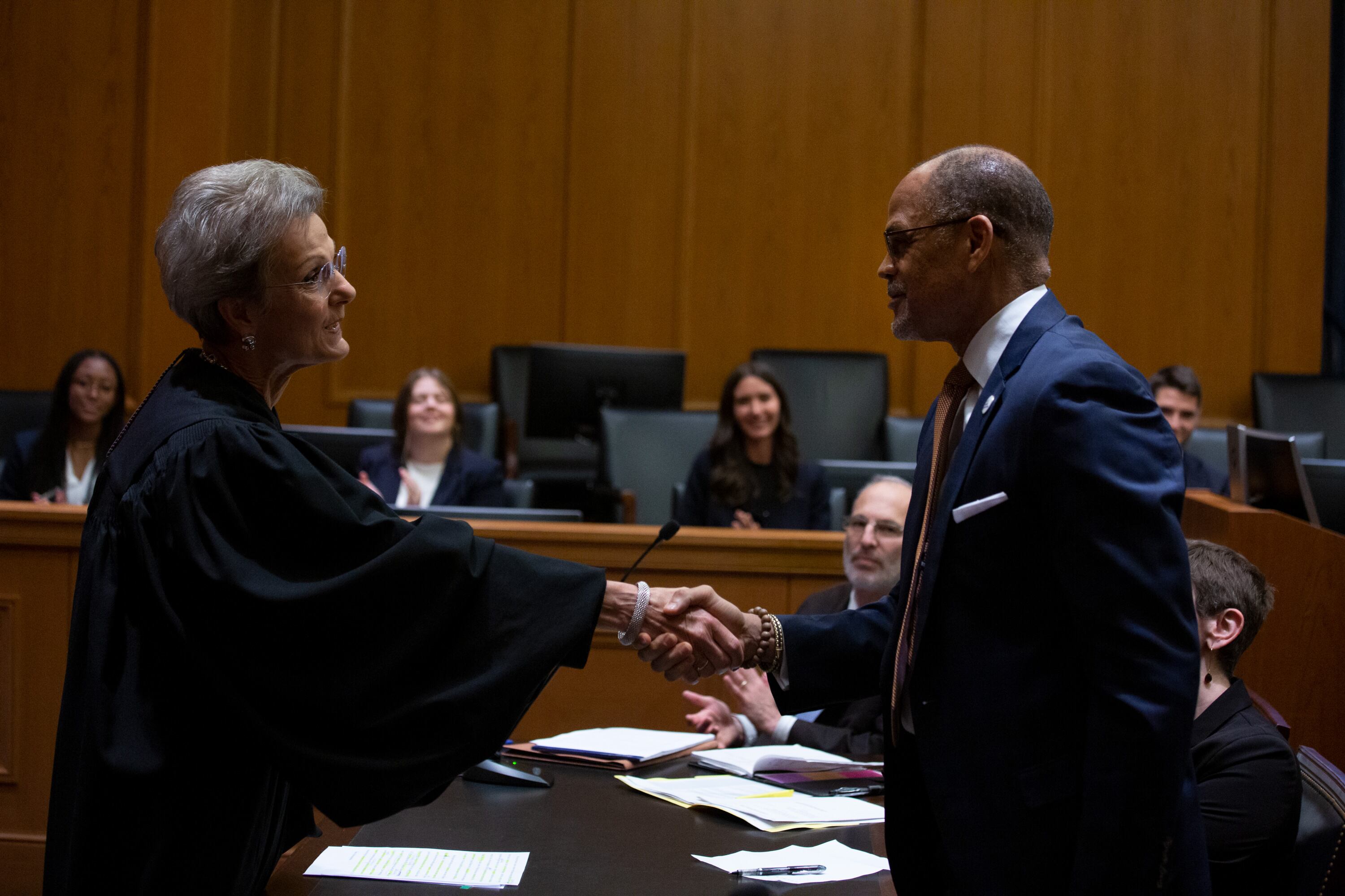 A woman in a black robe shakes hands with a man in a suit.