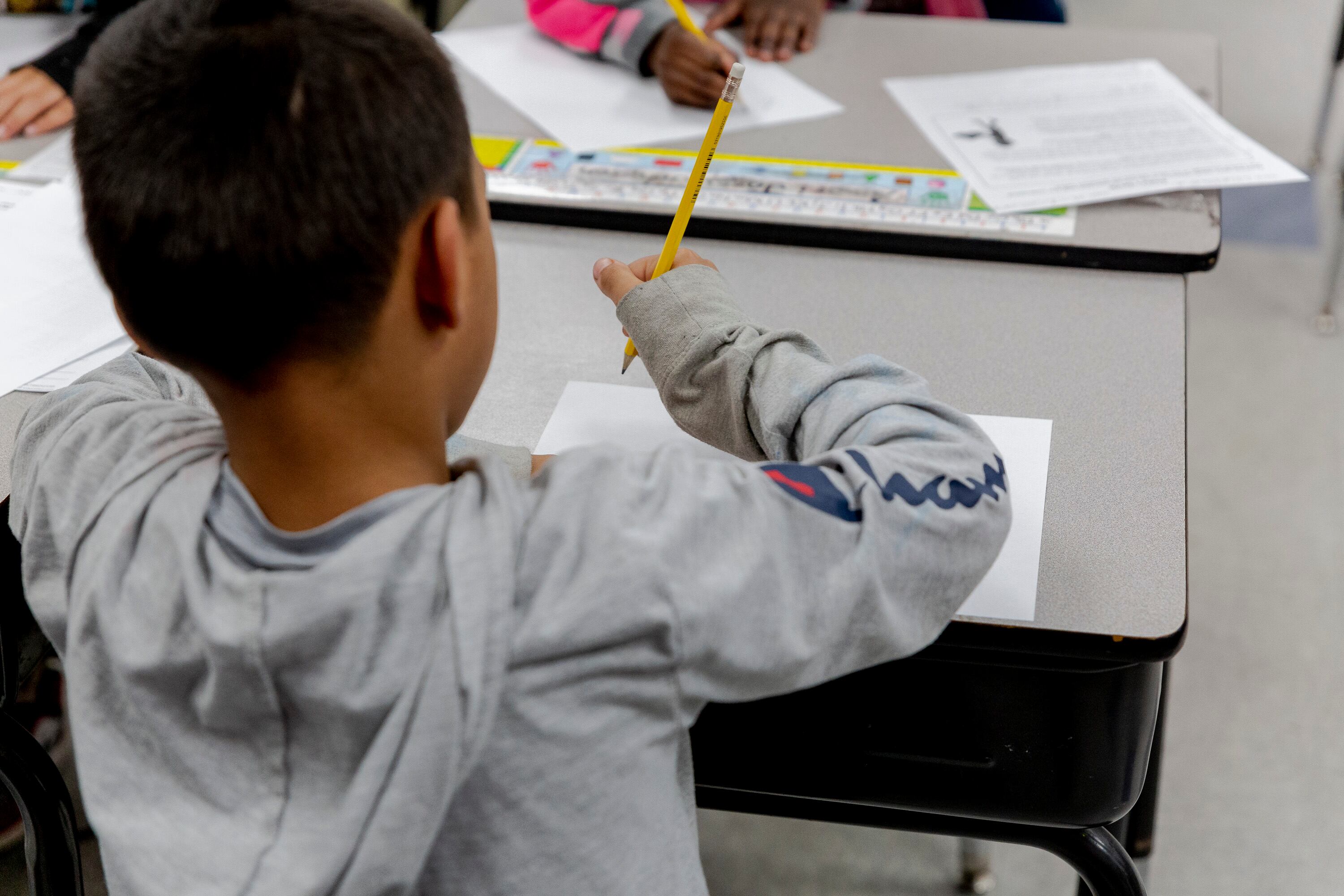 A boy wearing a gray Champion hoodie sits at a desk working on schoolwork.