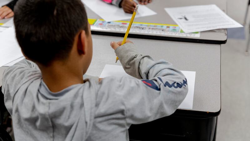 A boy wearing a gray Champion hoodie sits at a desk working on schoolwork.
