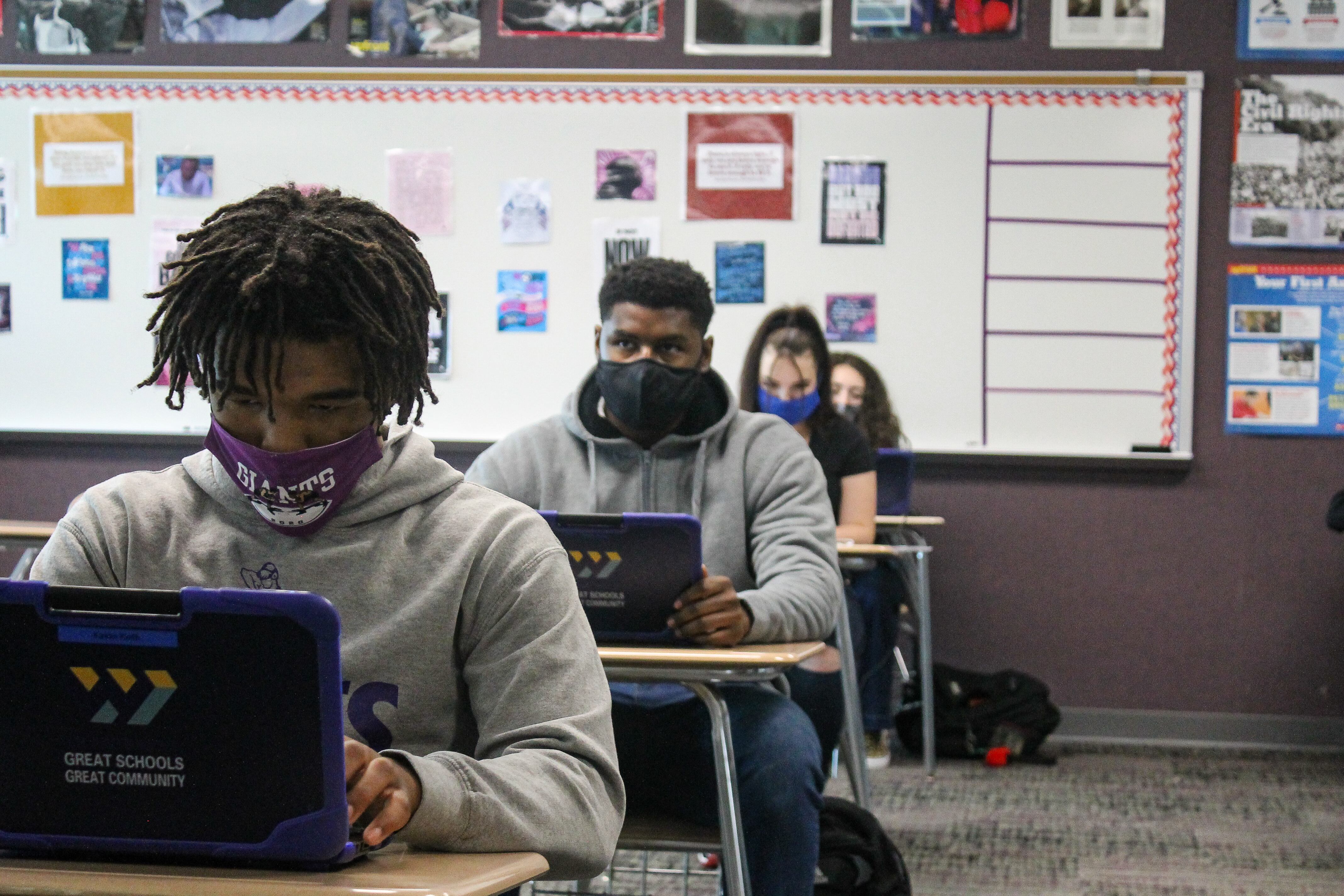 A row of masked students at Ben Davis High School in Indianapolis, Ind.,work on laptops in c classroom, with a white board behind them.