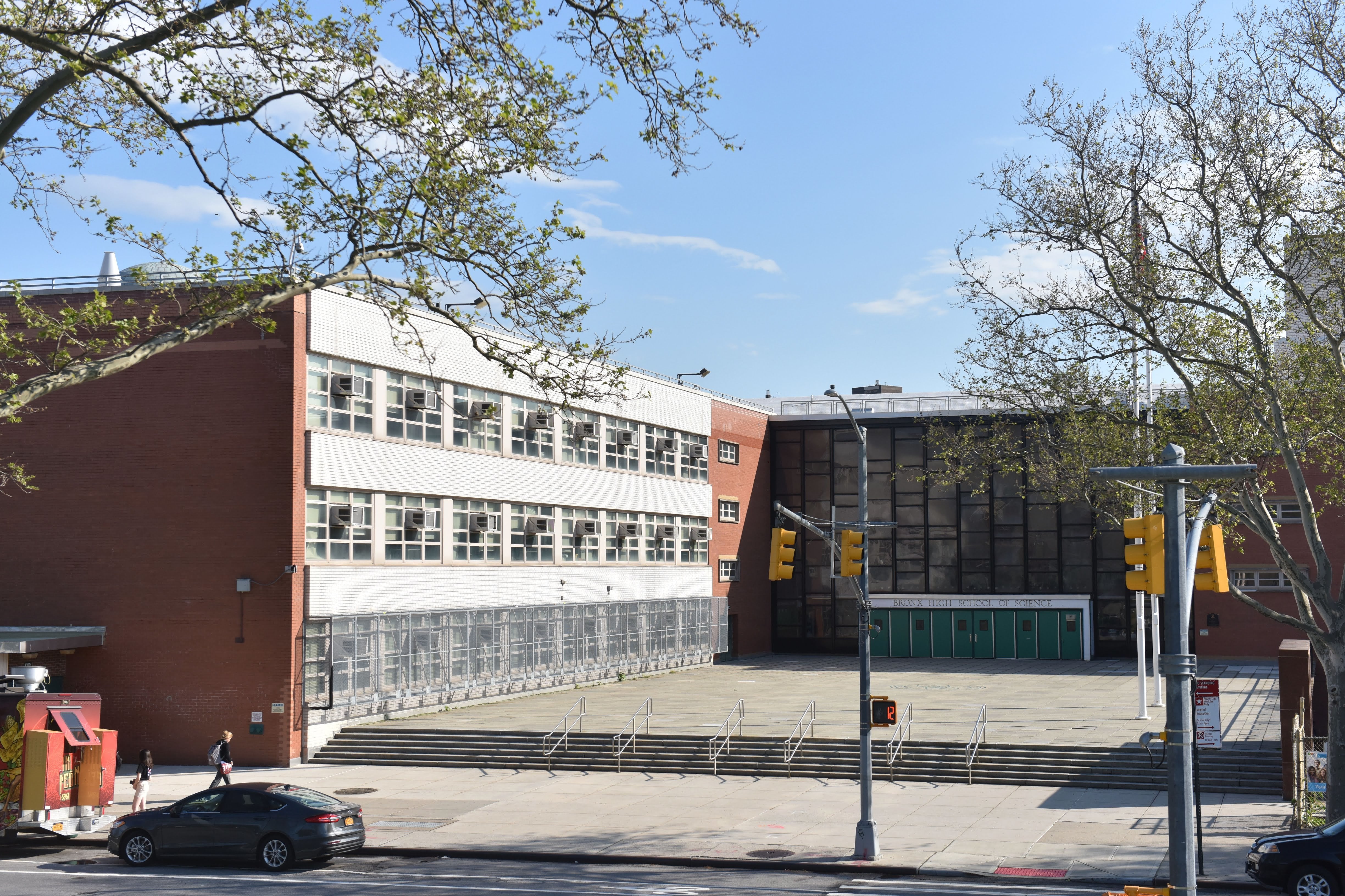 A white and brick building seen from a distance with trees on the edges.