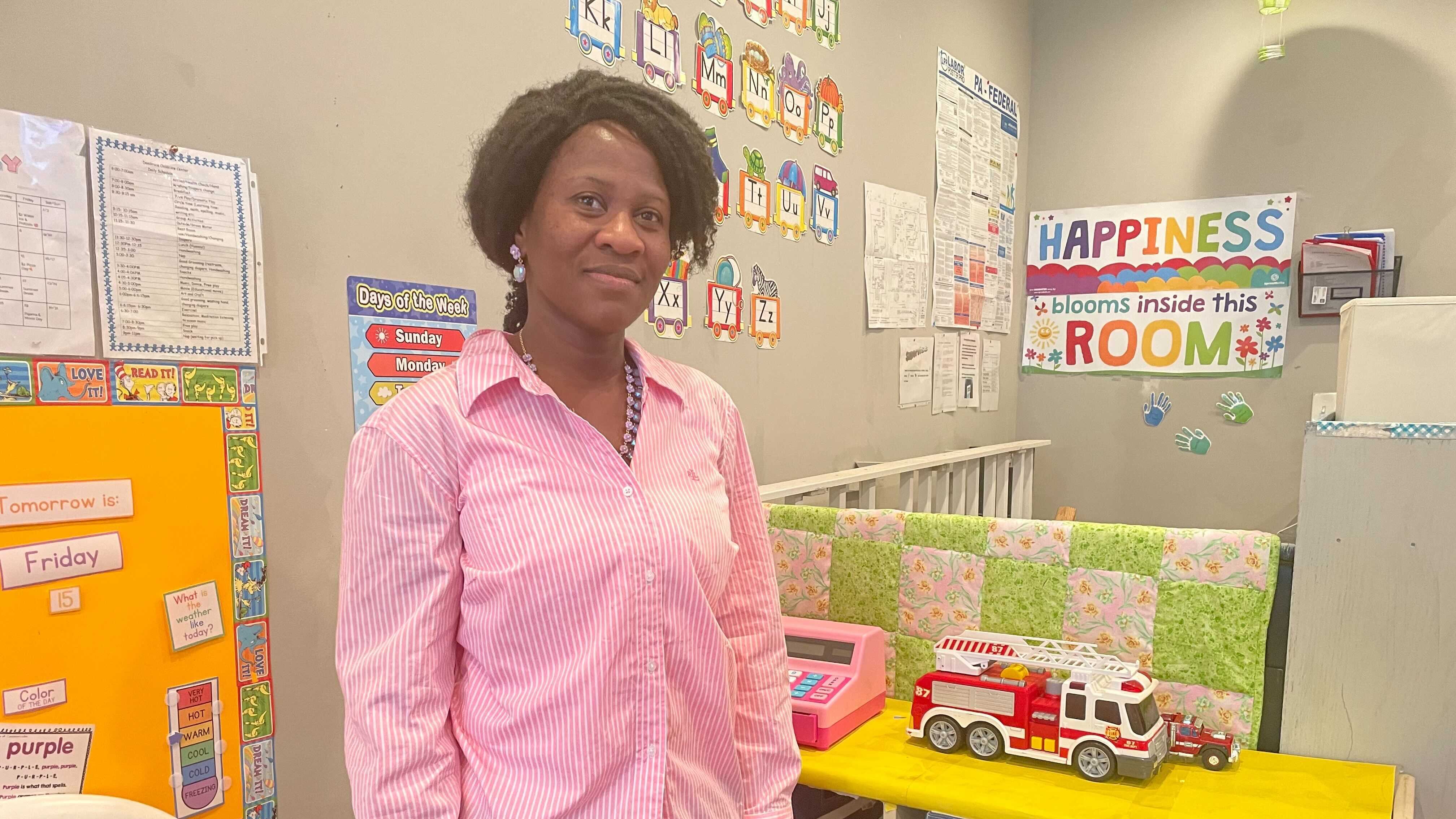 A woman in a pink shirt stands in a child care classroom.