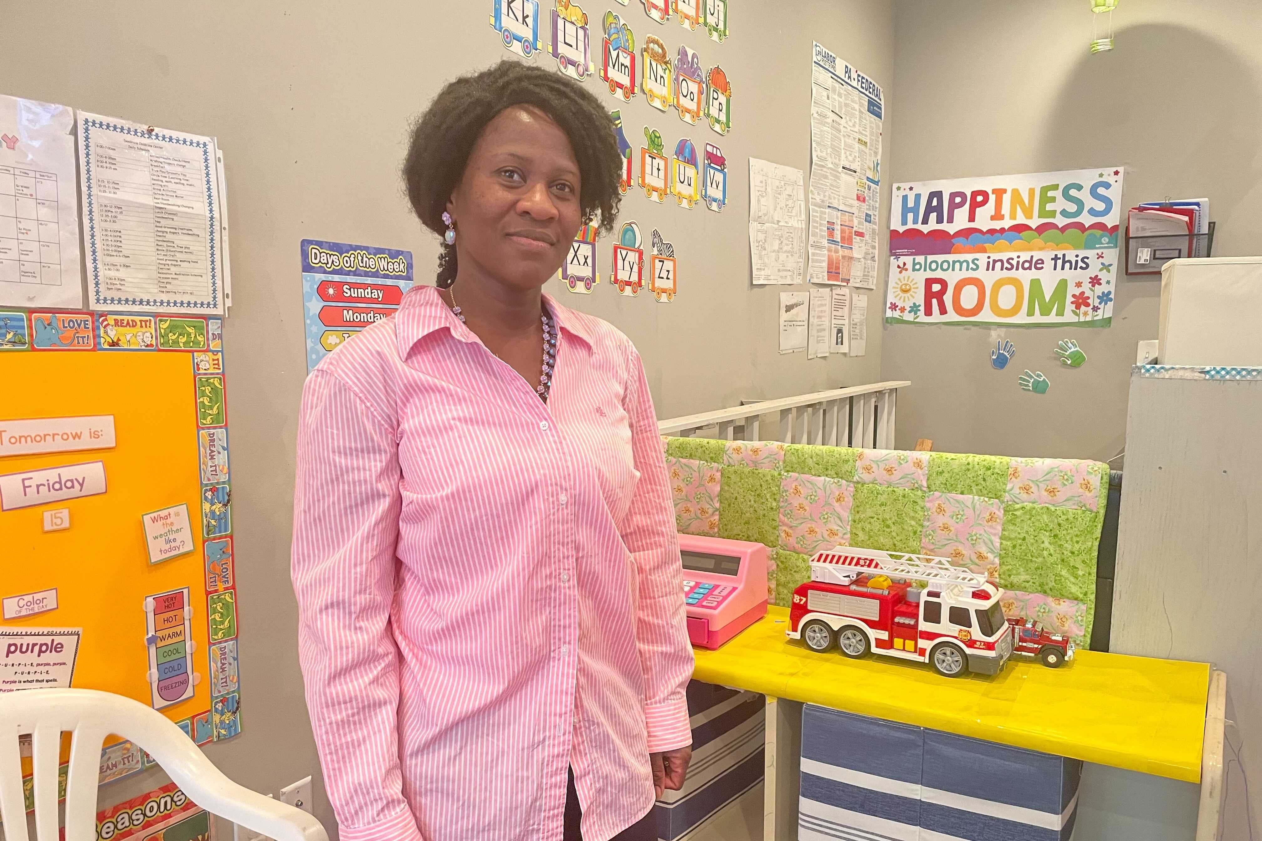 A woman in a pink shirt stands in a child care classroom.